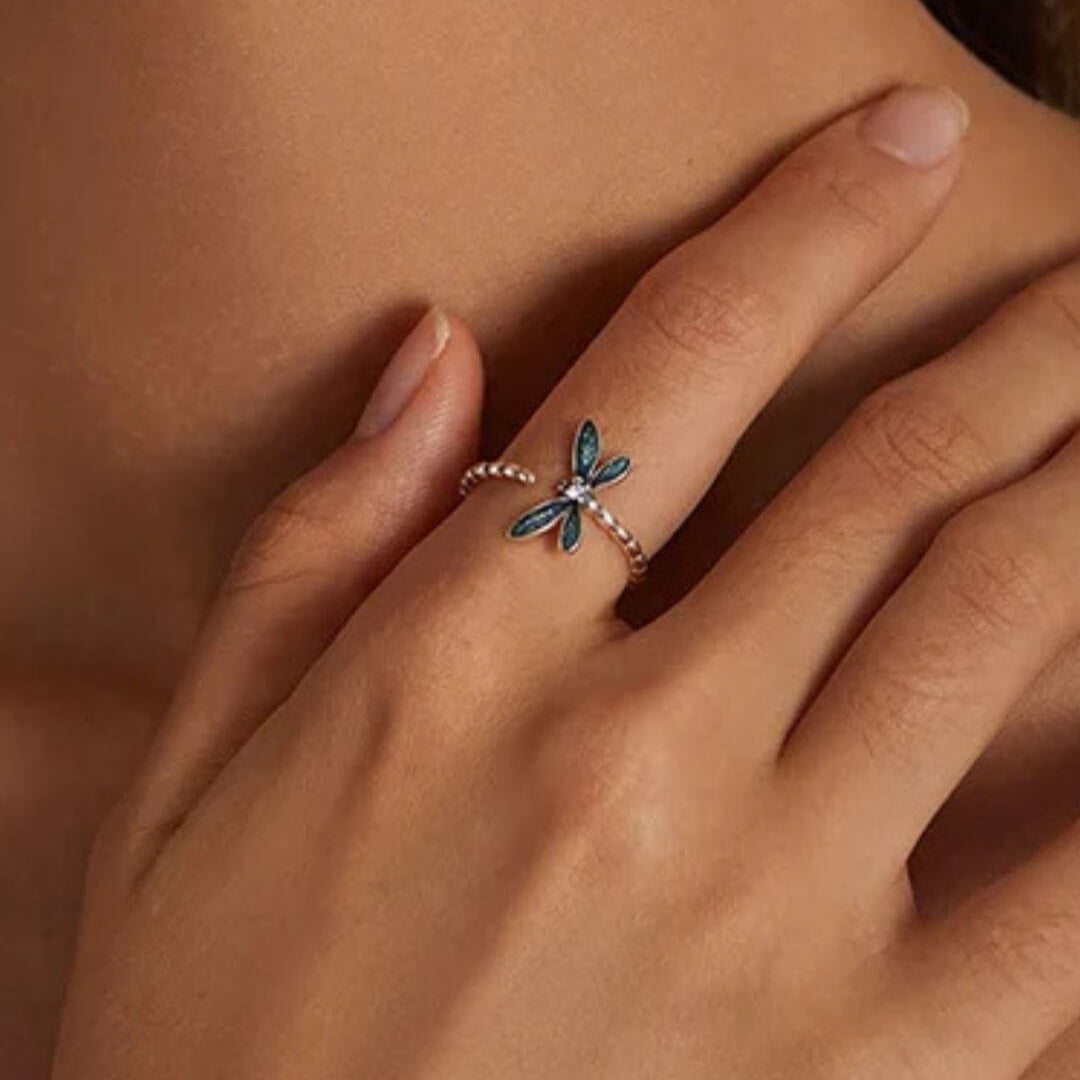 Close-up of a hand wearing a dragonfly-shaped ring on a neutral background