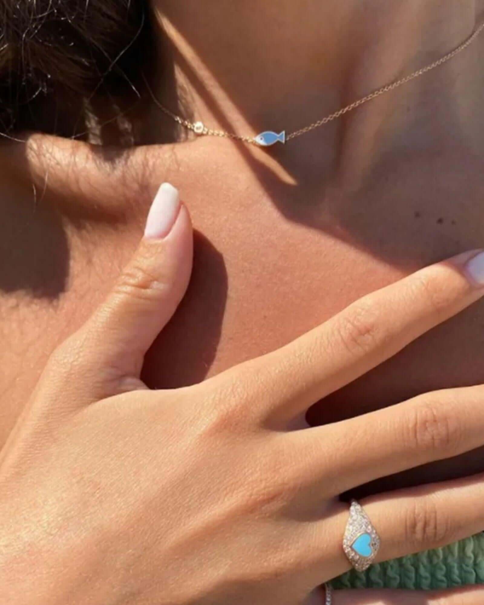 Close-up of a woman wearing a vintage fish pendant necklace and a matching ring with blue enamel accents.