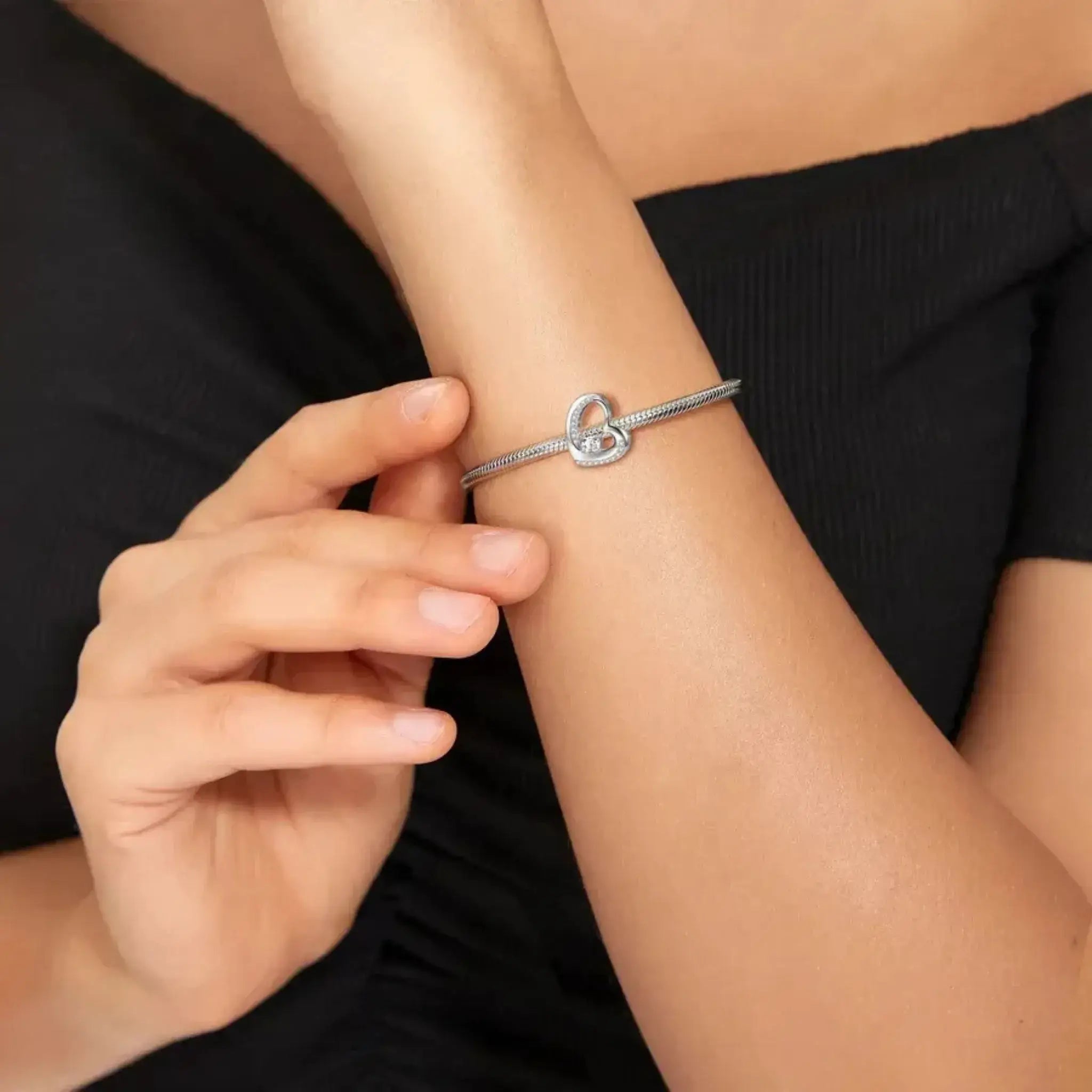 Close-up of a person wearing a silver bracelet with a heart clasp on a black background