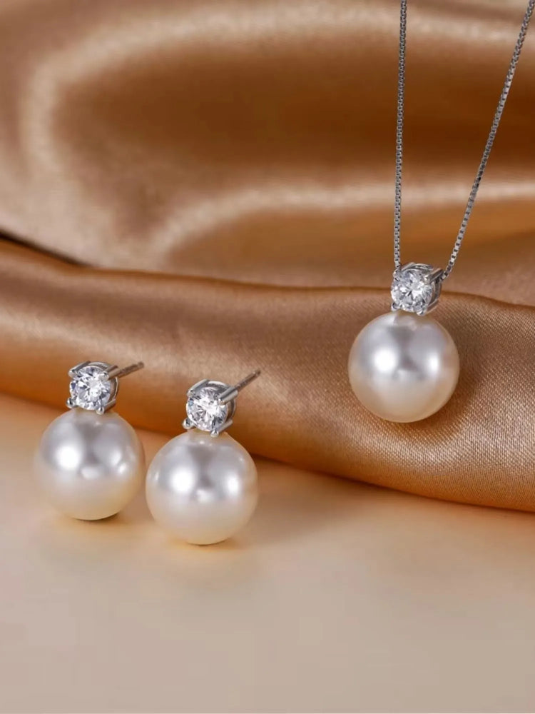 Elegant pearl necklace and earring set with zirconia, displayed on rich satin fabric.