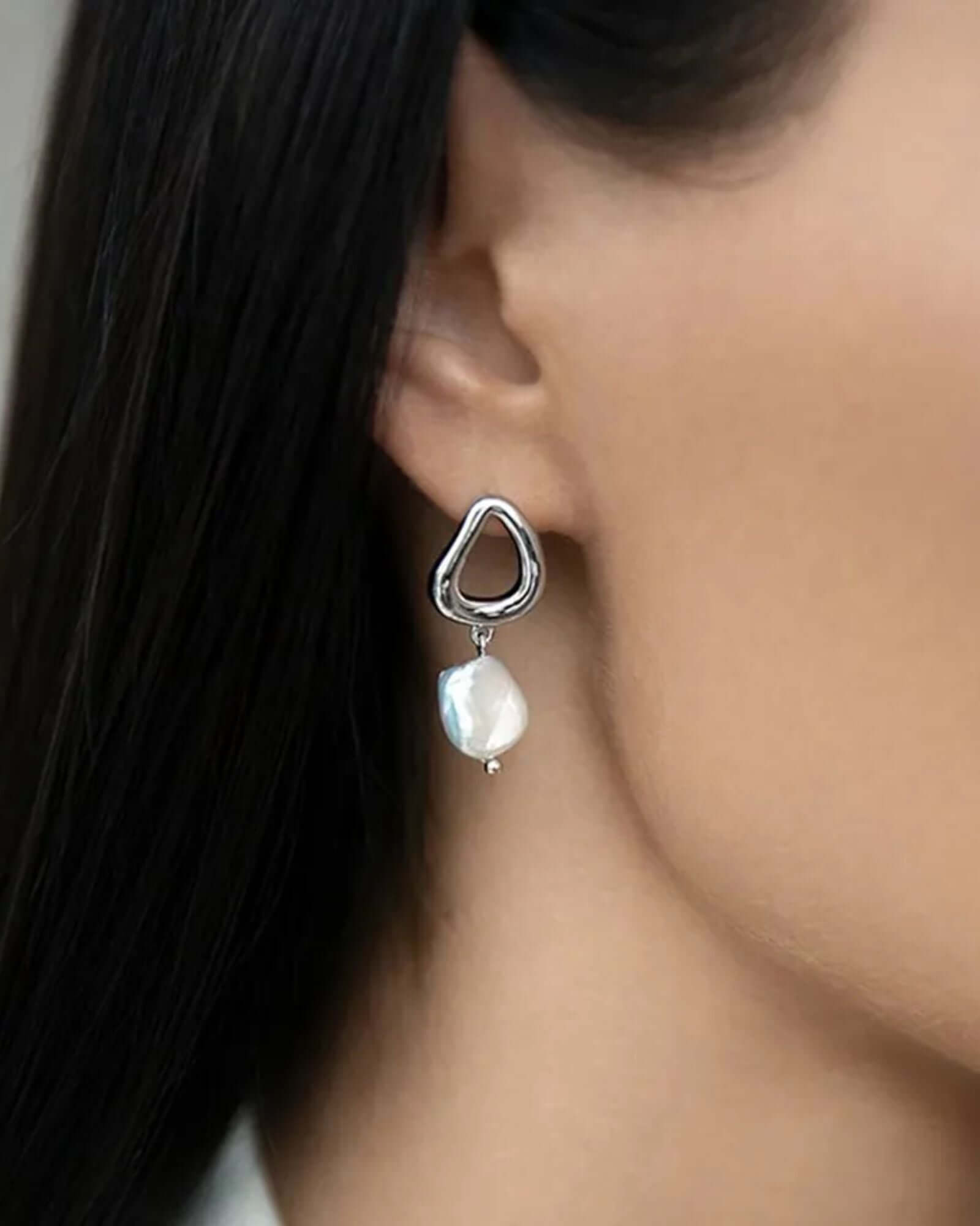 Earring with a heart-shaped metal clip and pearl drop worn by a person.