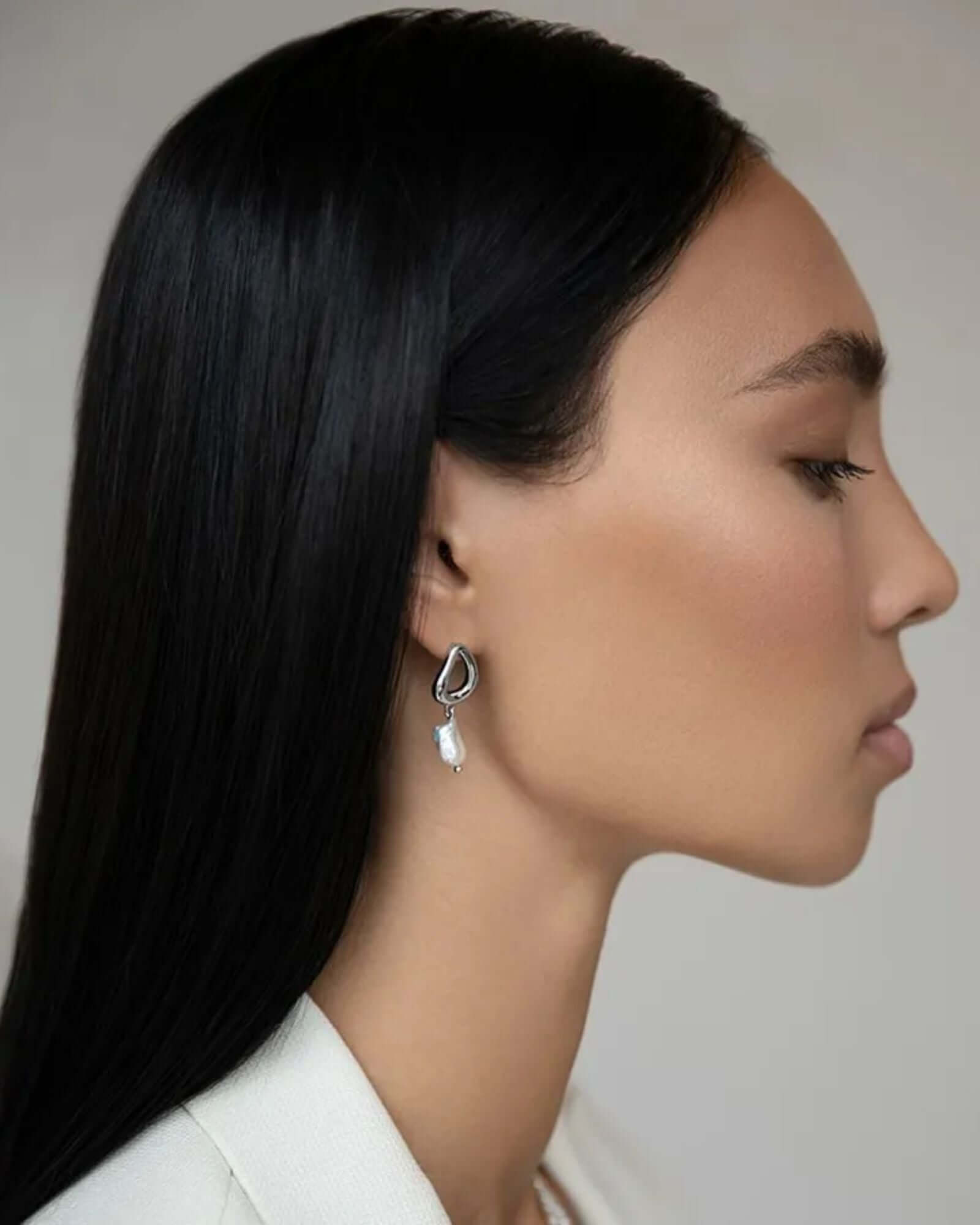 Woman wearing a silver earring with a white stone against a neutral background