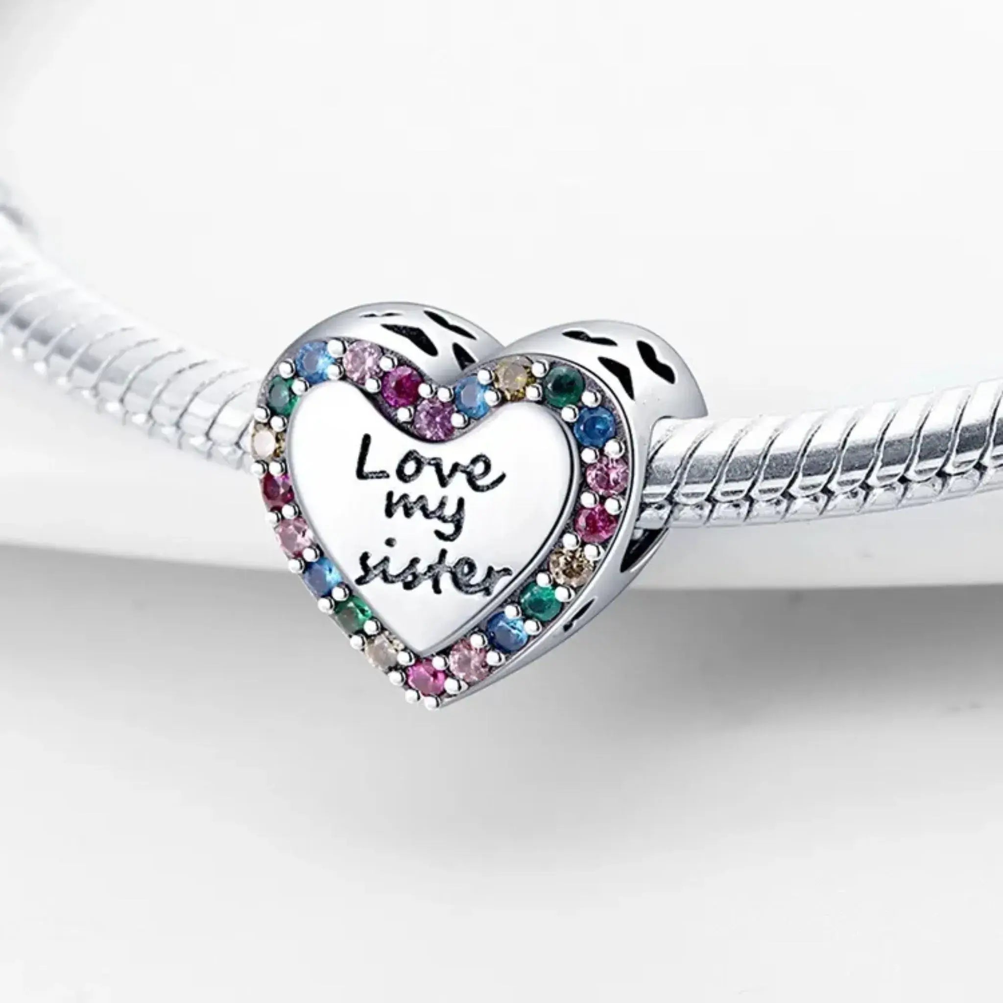 Silver heart-shaped charm with 'Love my sister' engraving and colorful stones on a white background