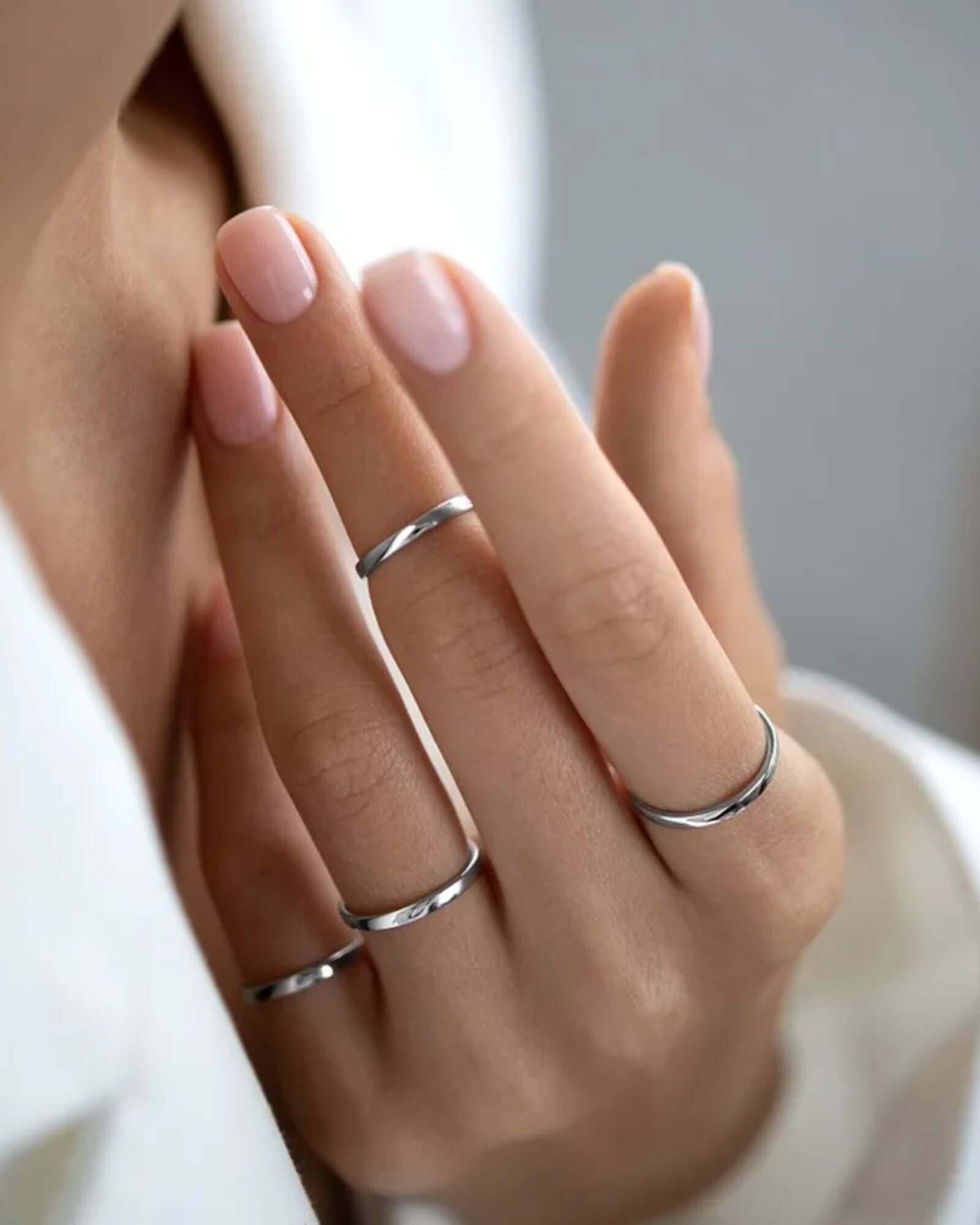 Elegant display of a hand wearing multiple plain silver rings, showcasing timeless simplicity and beauty.