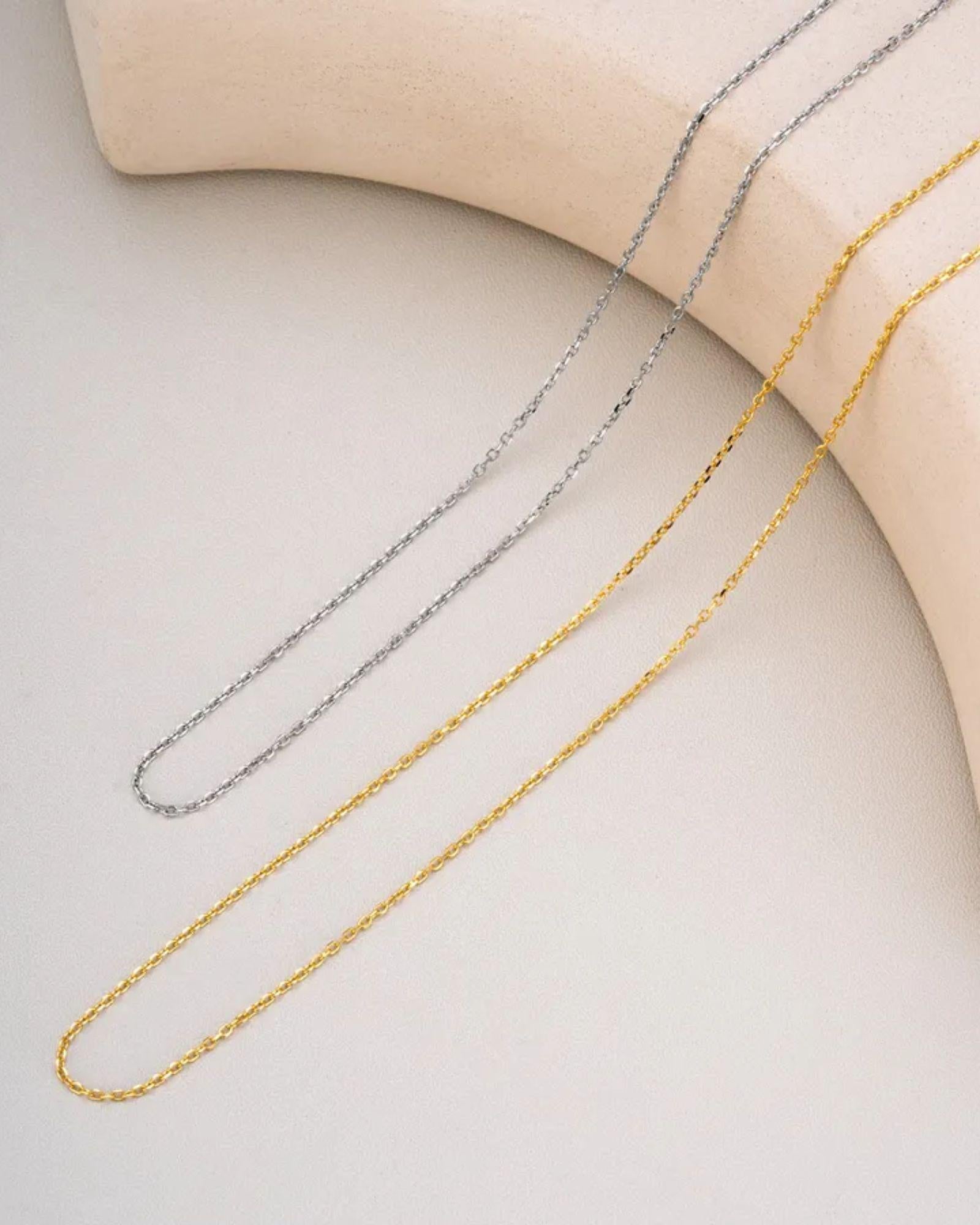 Simple silver cable chain alongside other chains on a neutral surface, showcasing versatility and elegance.