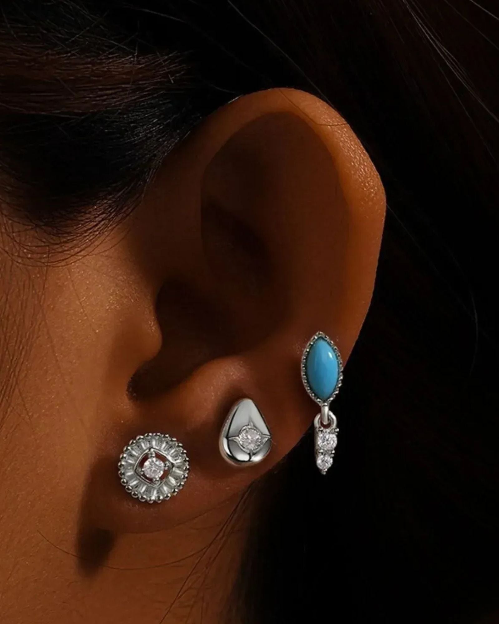 Close-up of an ear wearing three earrings against a dark background