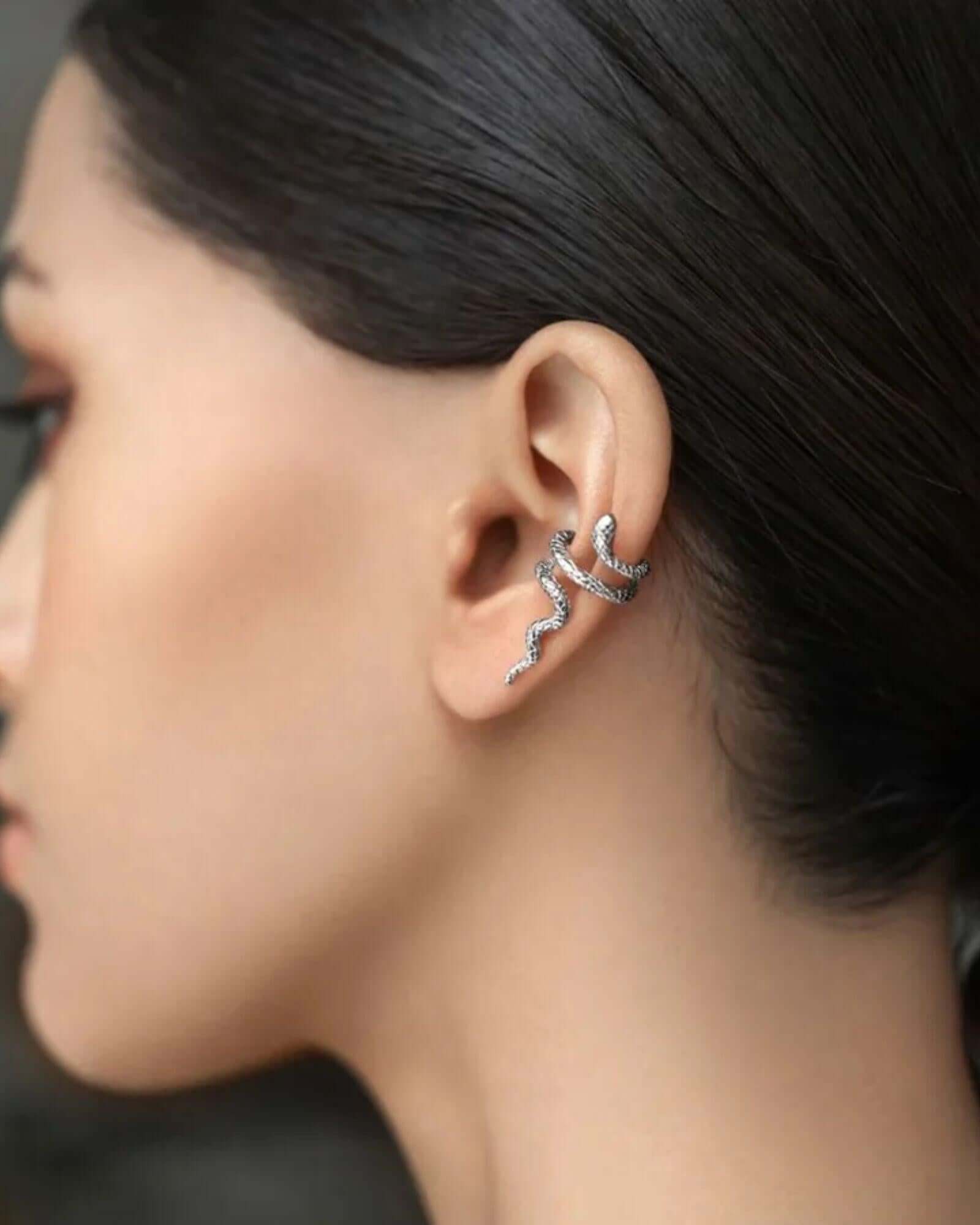 Close-up of an ear with a silver earring against a neutral background