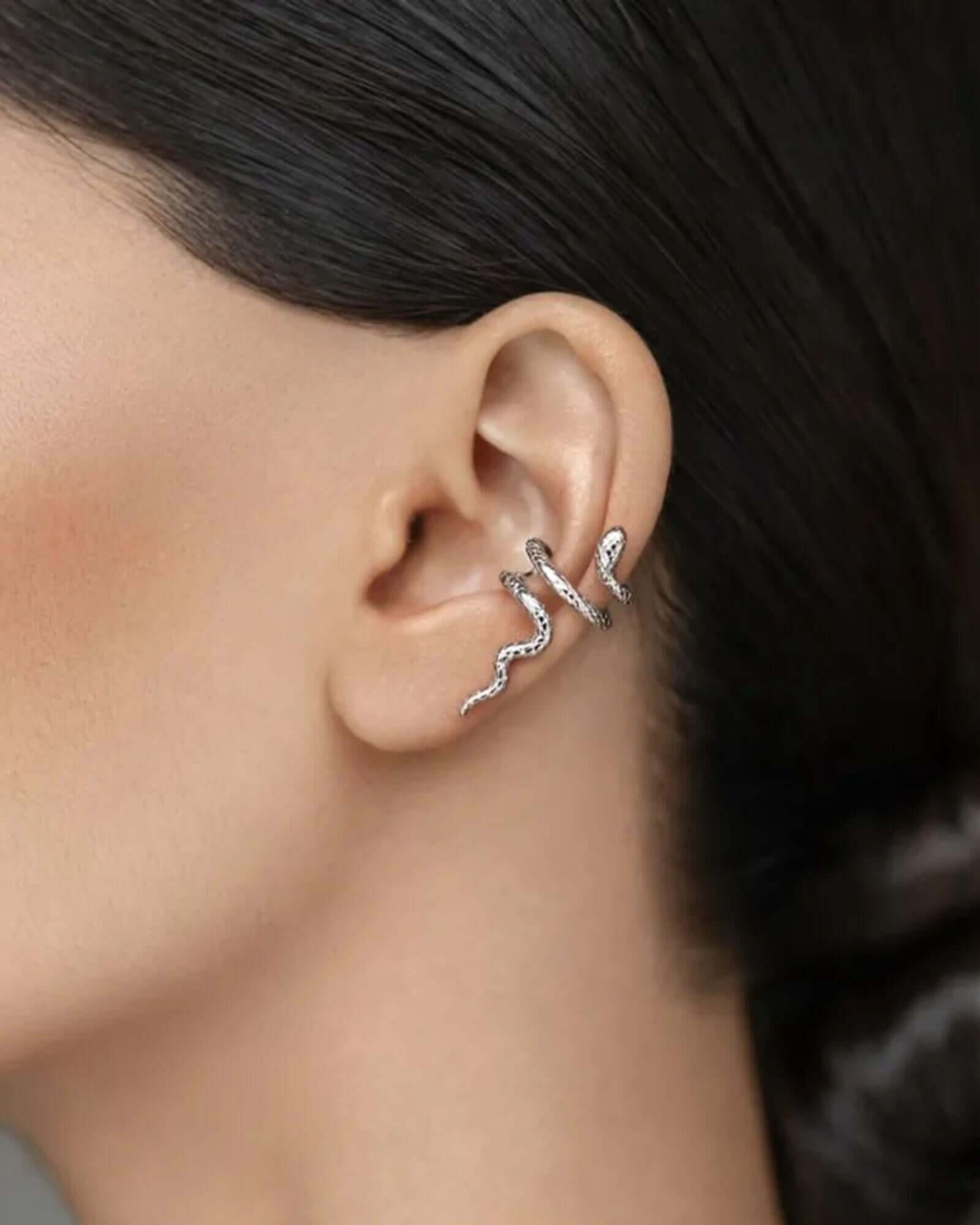 Close-up of an ear wearing a silver earring with dark hair and skin background