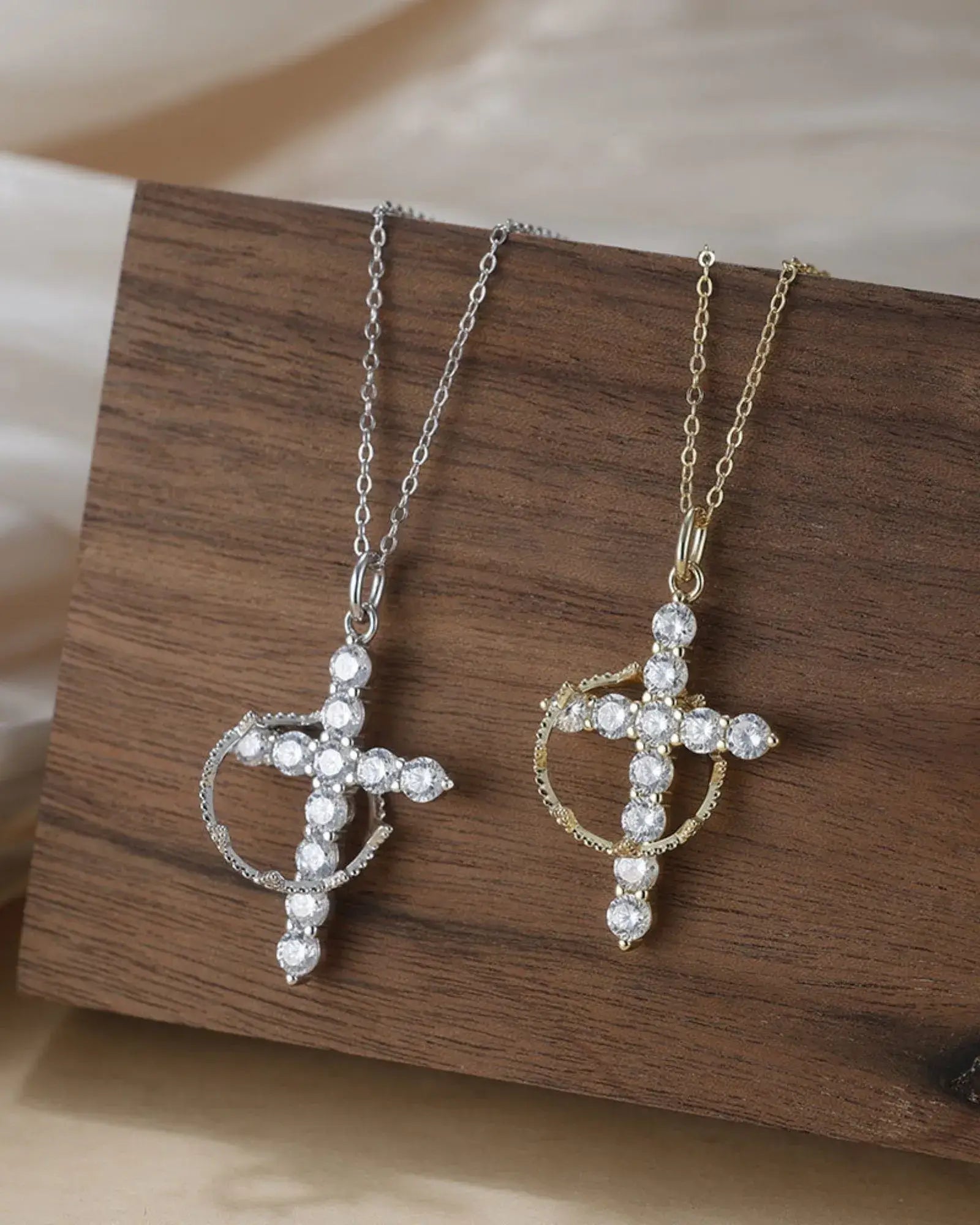 Elegant Faith pendant necklace in silver and gold, featuring a cross design with sparkling gems on a wooden display.