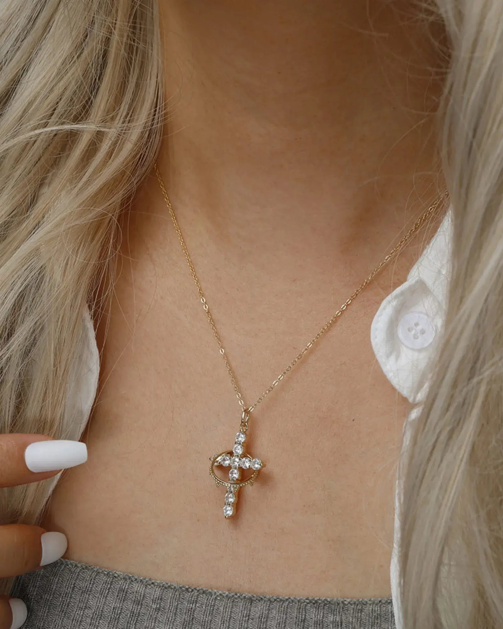 Stylish gold Faith pendant necklace with cross and crown design, worn over a grey top.