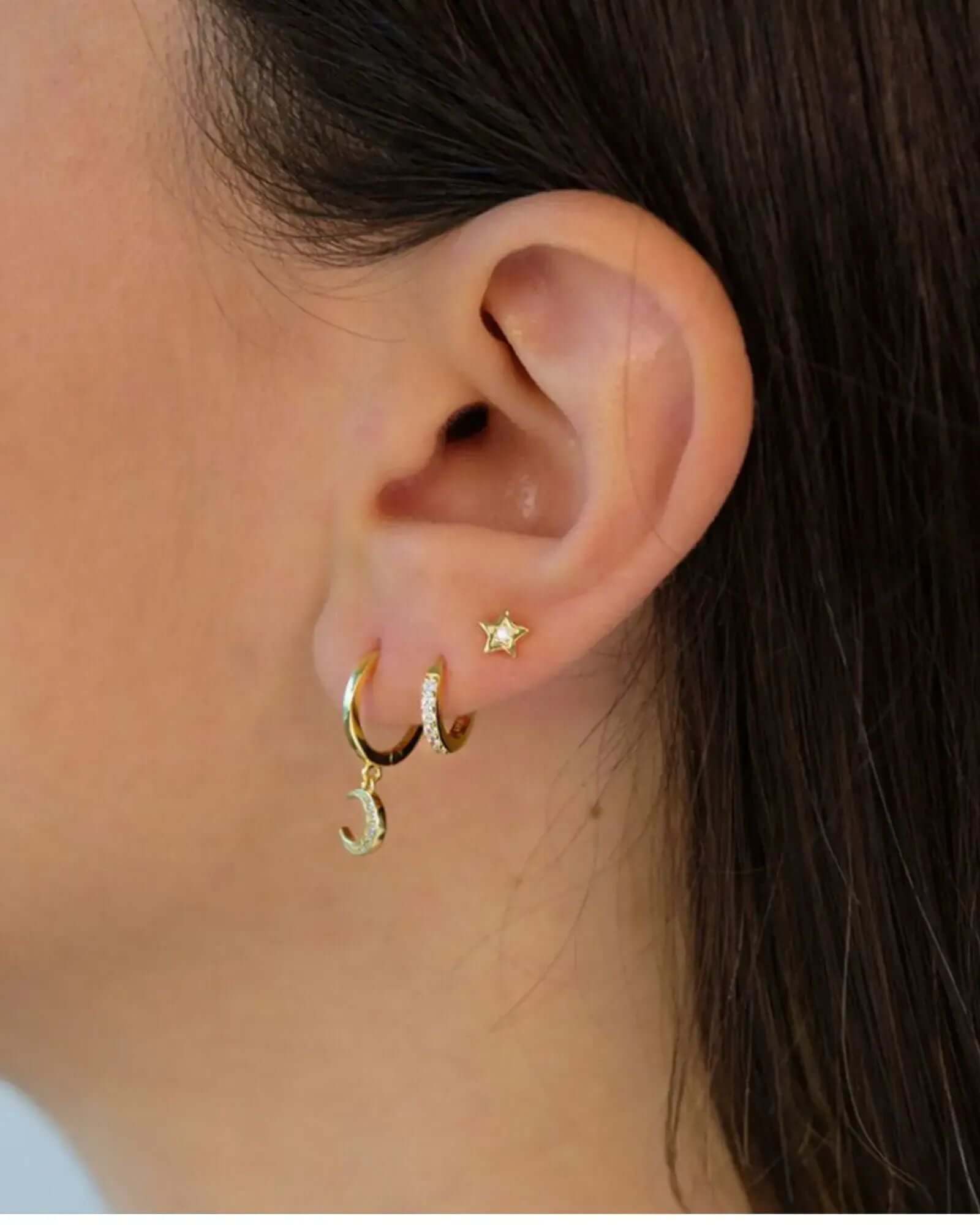 Close-up of a model's ear wearing a three-piece earring set with gold hoops and a star stud.