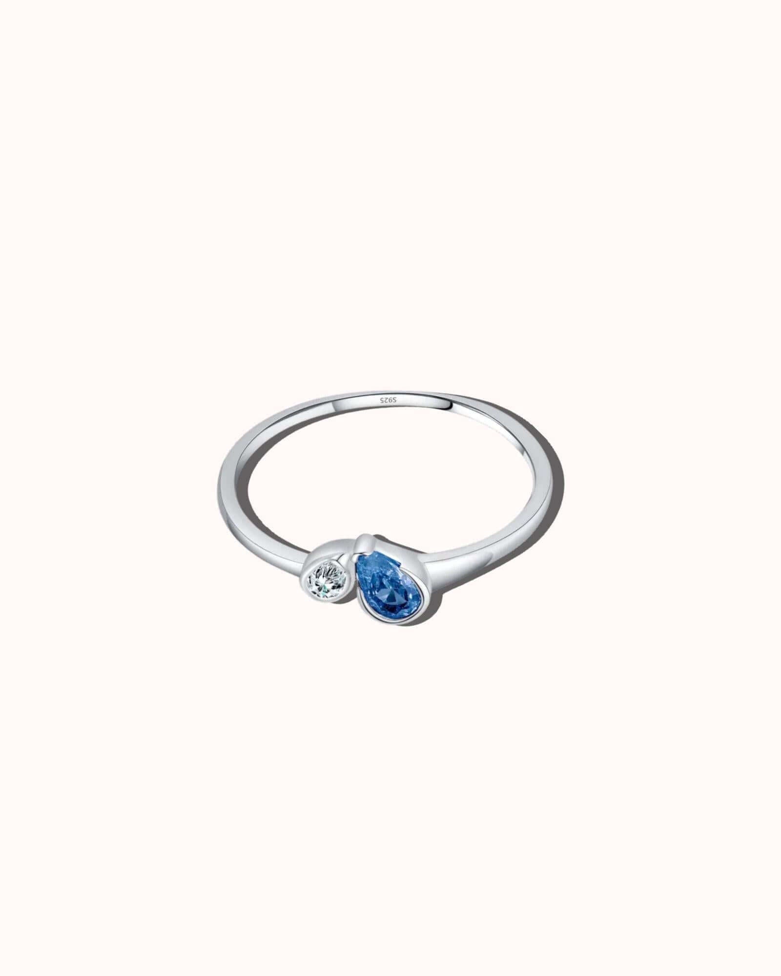 Silver ring with a blue gemstone and smaller clear gemstone on a white background