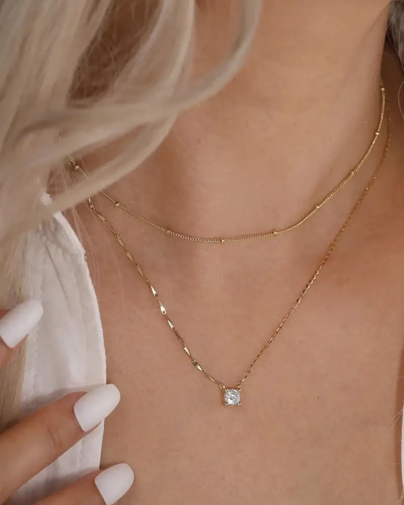 Close-up of a woman wearing a Bling pendant Necklace with a cubic zirconia pendant and layered gold chains.