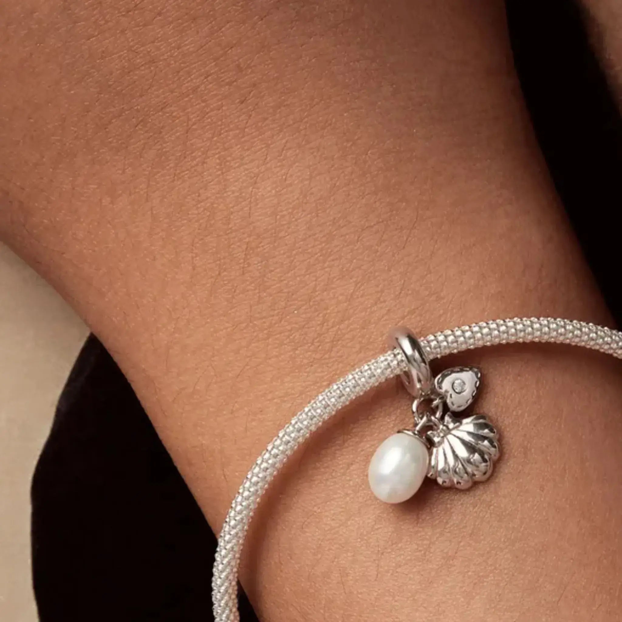 Close-up of a bracelet with a pearl and shell charm on a wrist.