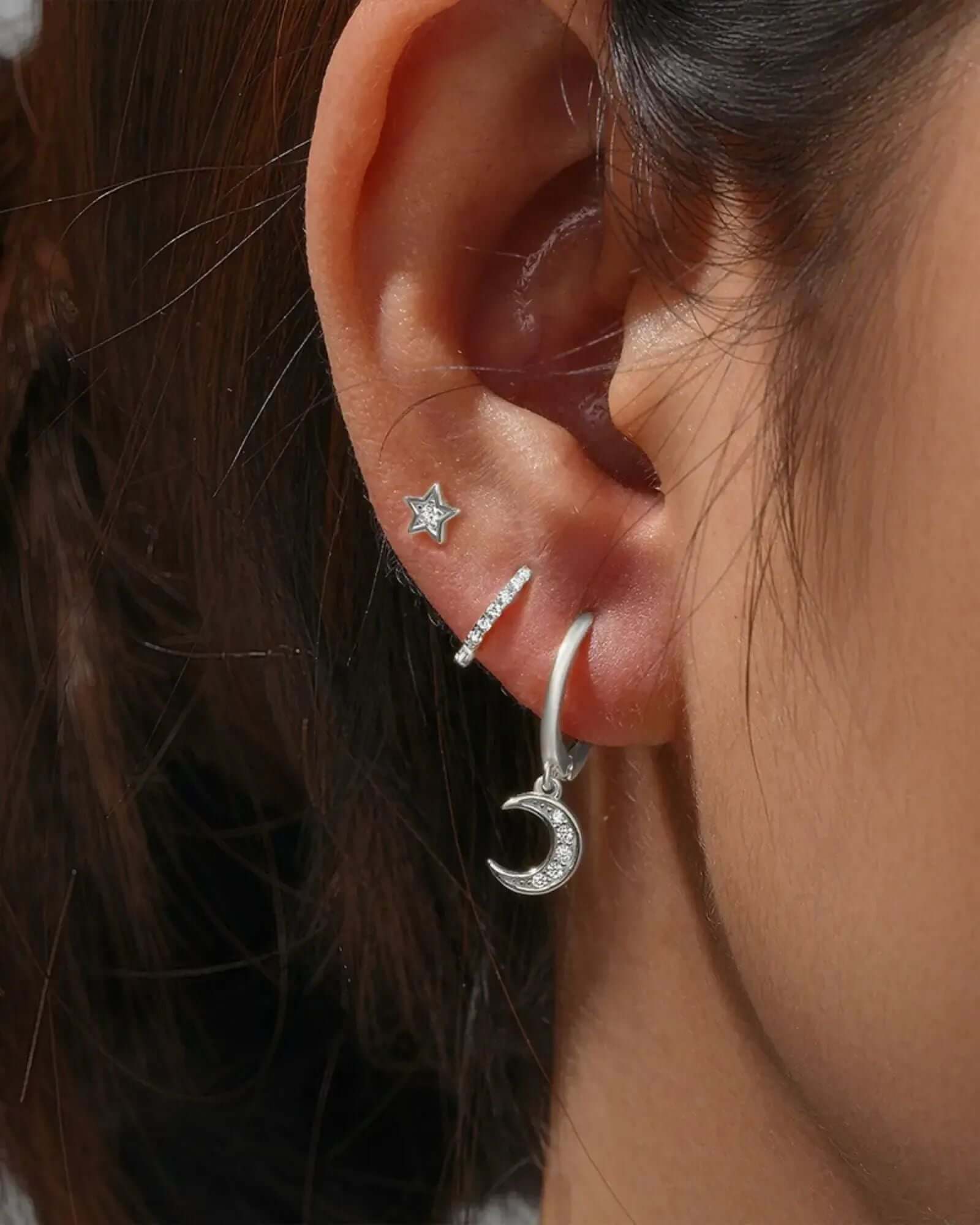 Close-up of a woman's ear showcasing a three-piece sterling silver earring set with star and moon designs.