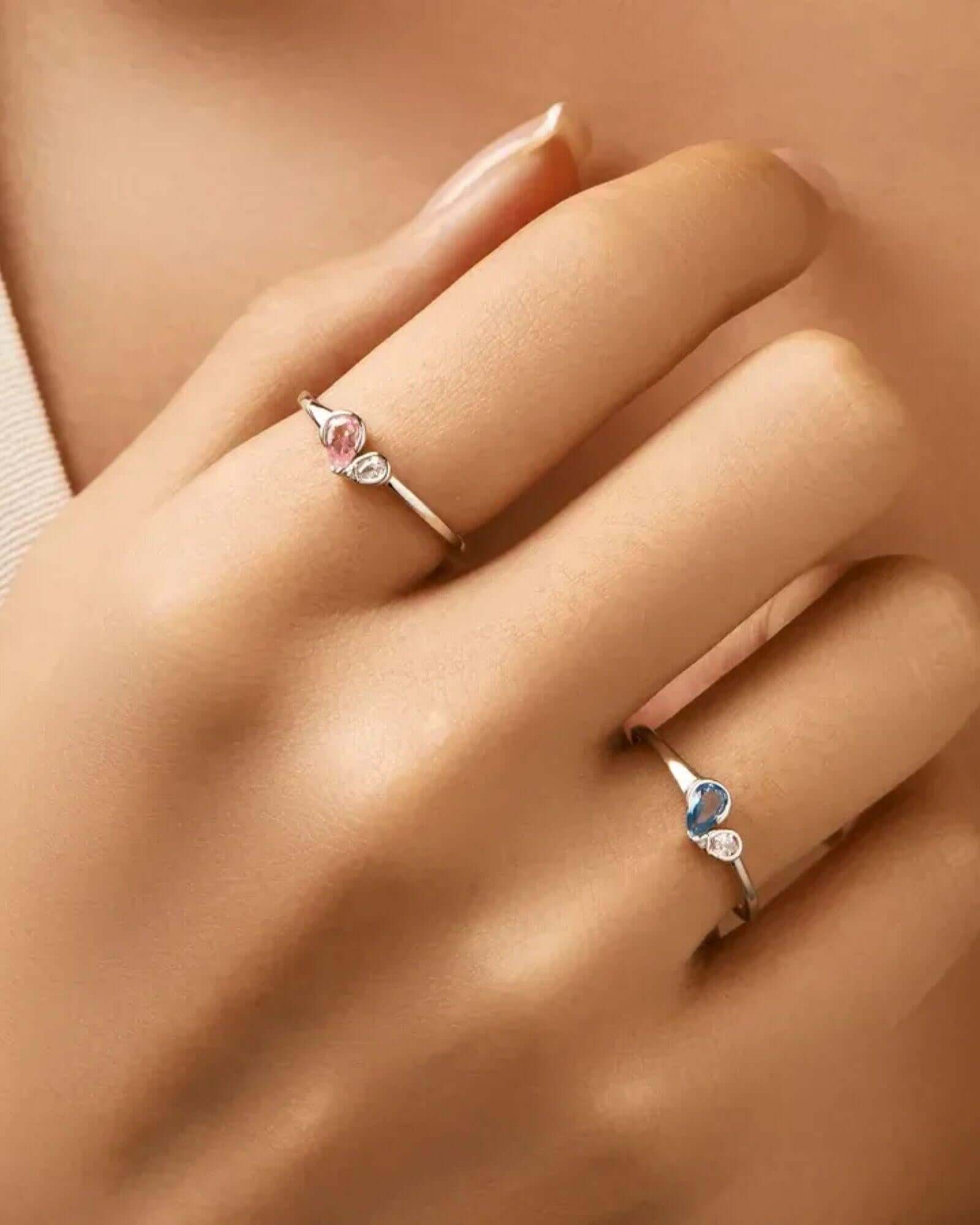 Close-up of a hand wearing two rings with gemstones on a neutral background