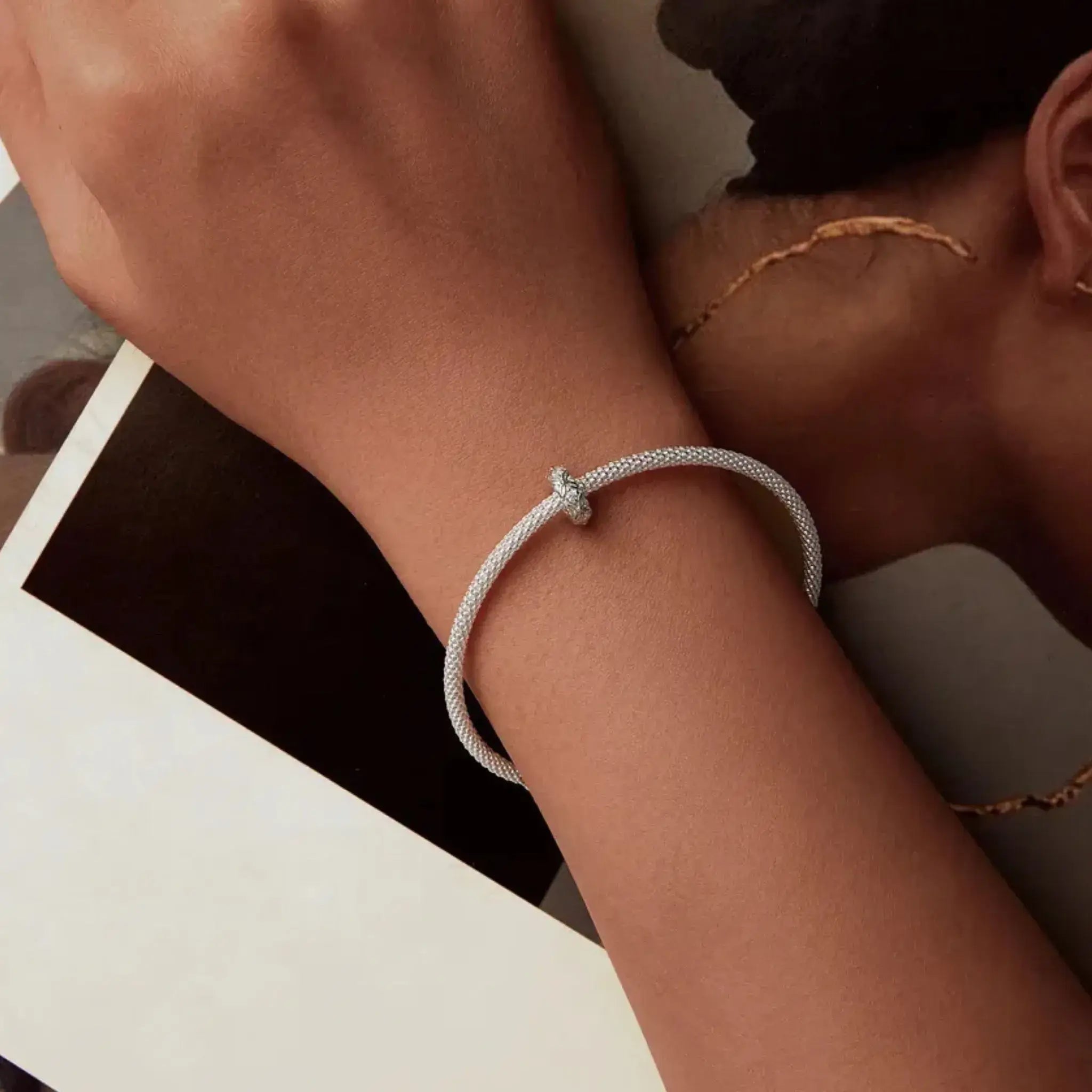 Close-up of a wrist wearing a silver bracelet with a minimal background