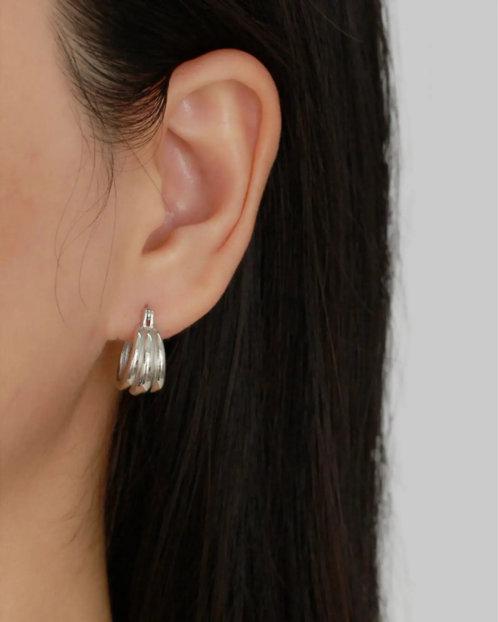 Sleek Aura Curve Hoop Earring in polished silver worn on an ear, showcasing its wave-like curves and geometric design.