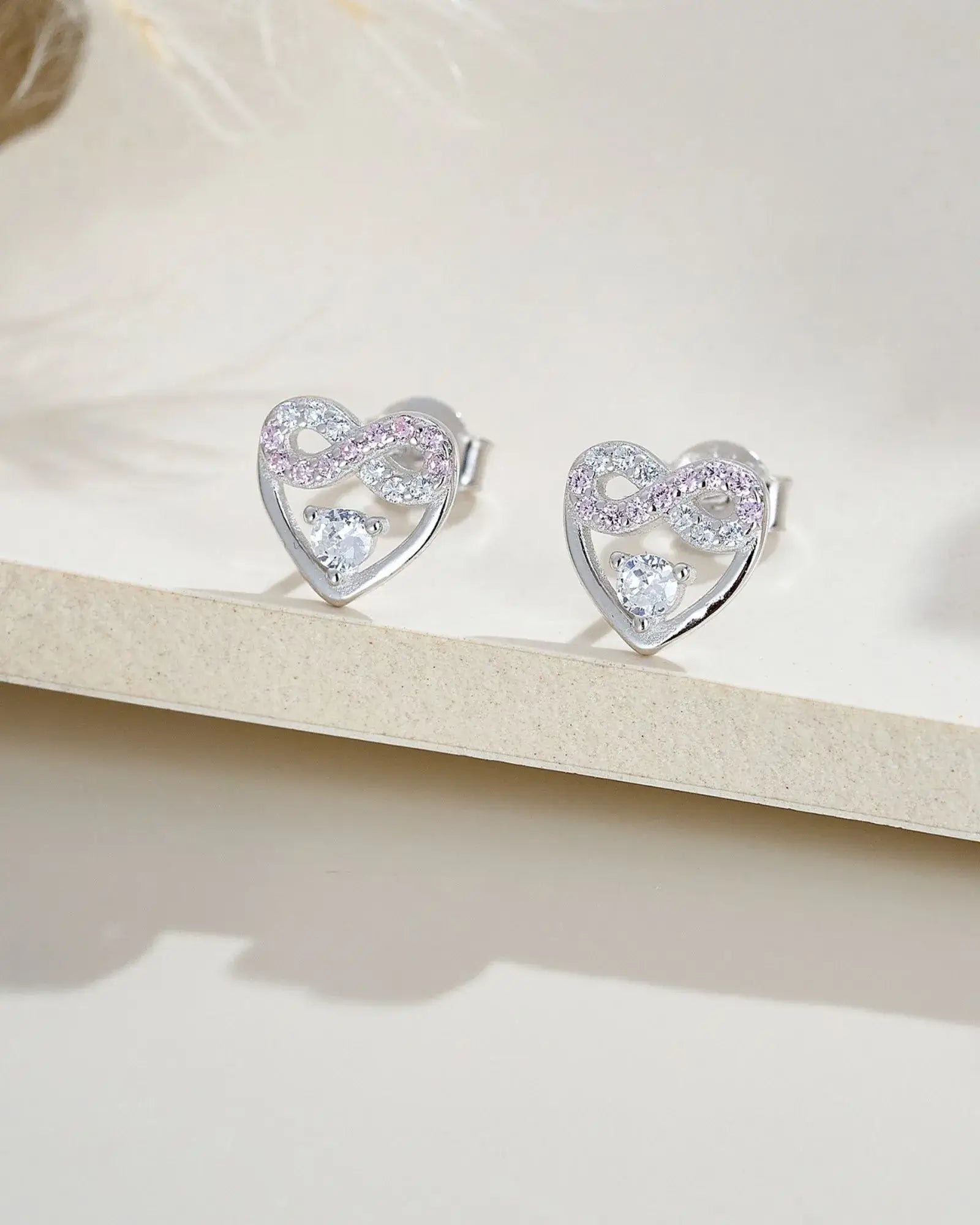 Eternal Blush Heart Ear Studs in sterling silver with infinity symbol and pink-white stones, showcasing timeless elegance.