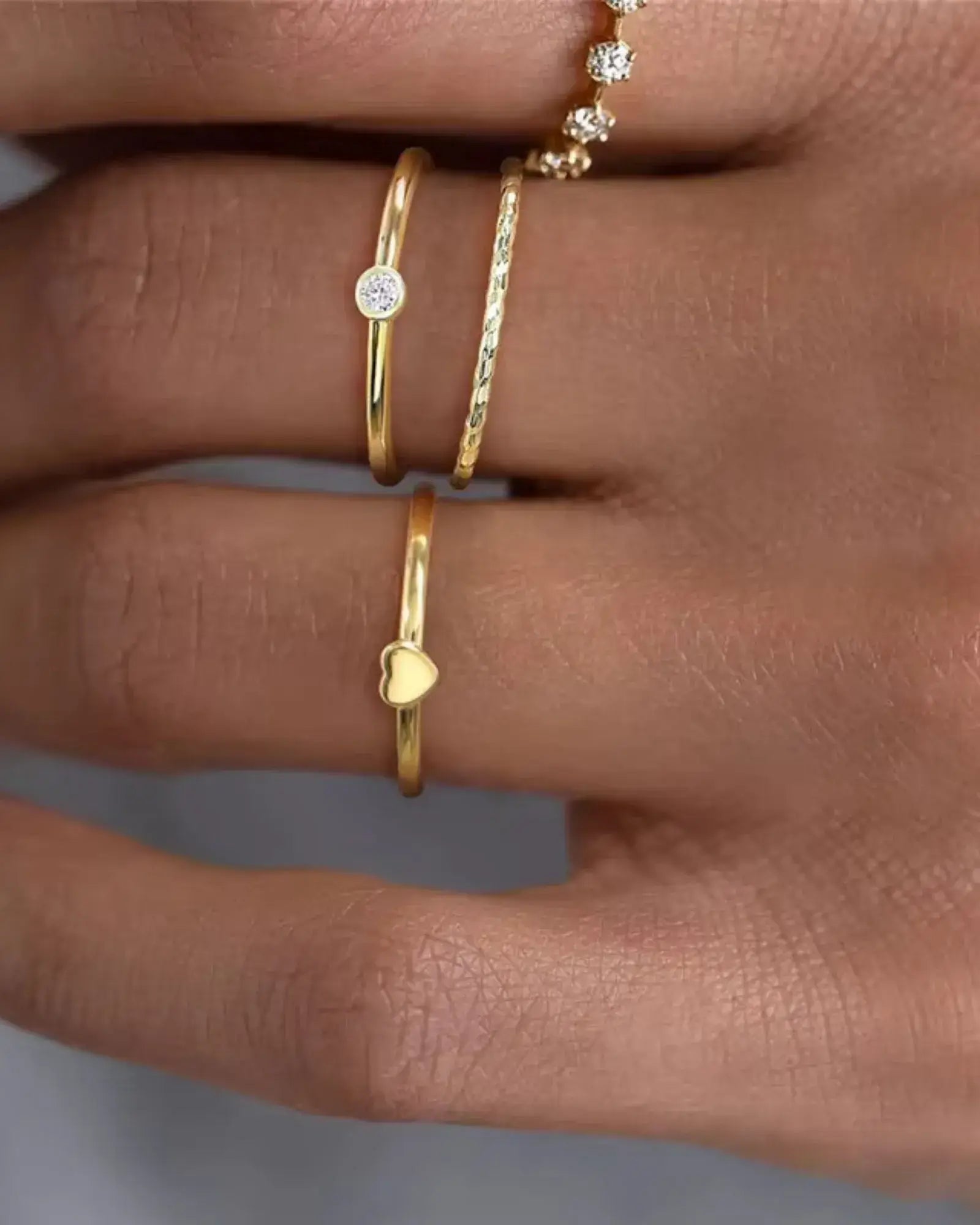 Golden Whisper Rings featuring a cubic zirconia bezel, textured band, and heart shaped design on a hand.