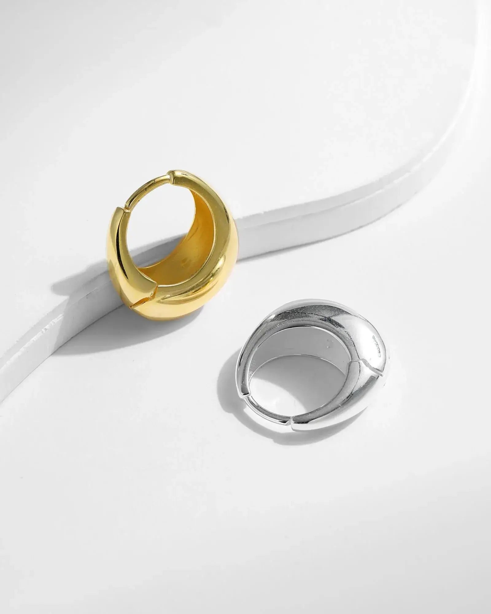Elegant gold and silver irregular solid hoop earrings showcasing modern design on a minimalist background.