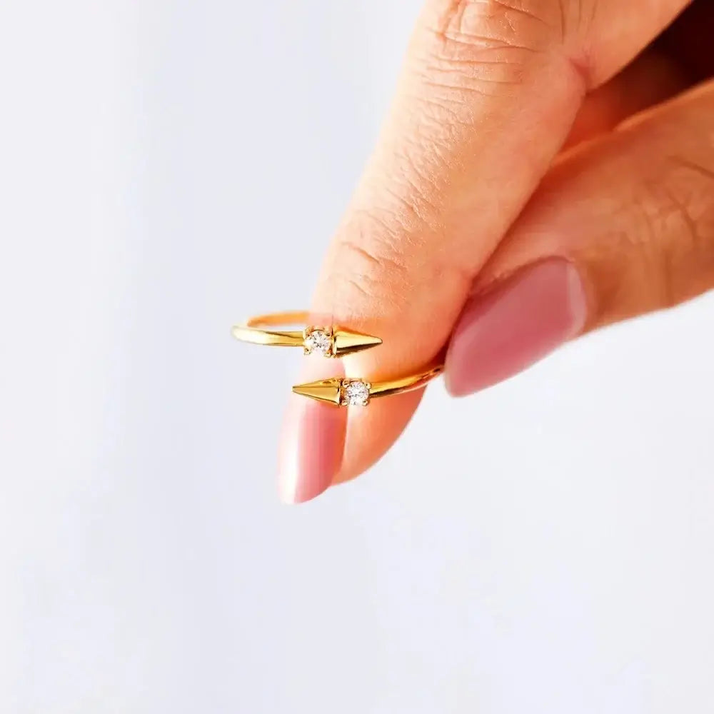 Open Arrow Ring in gold held between fingers, featuring cubic zirconia accents on stylish design.