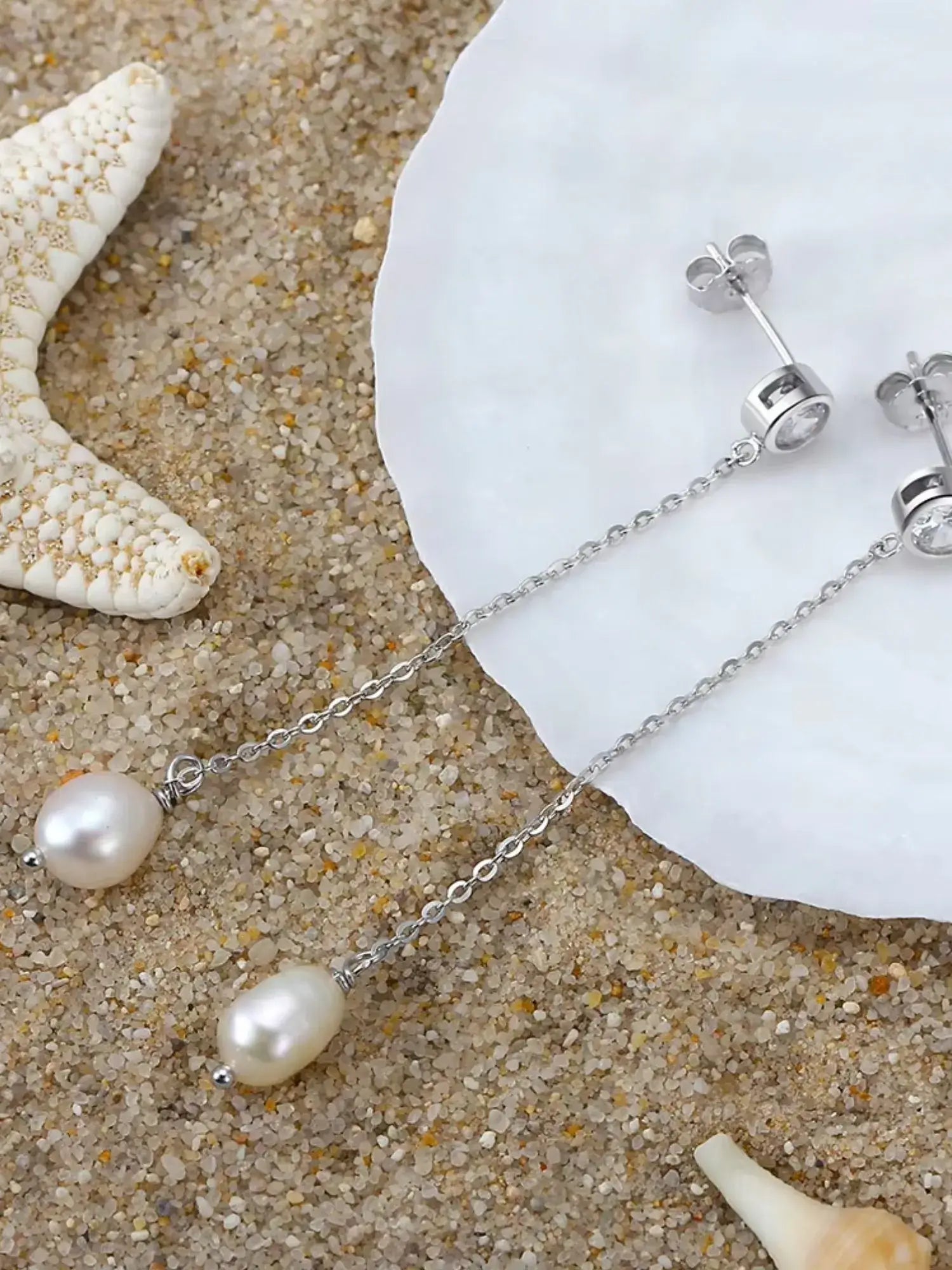 Elegant silver pearl drop earrings resting on sandy beach, highlighting their grace and sophistication.