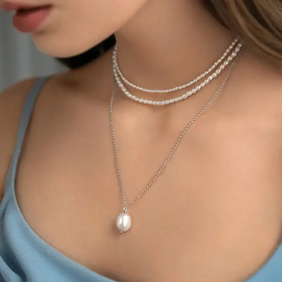 Close-up of a woman wearing the Lumera Pearl Set necklace with multiple strands of pearls on a blue top.