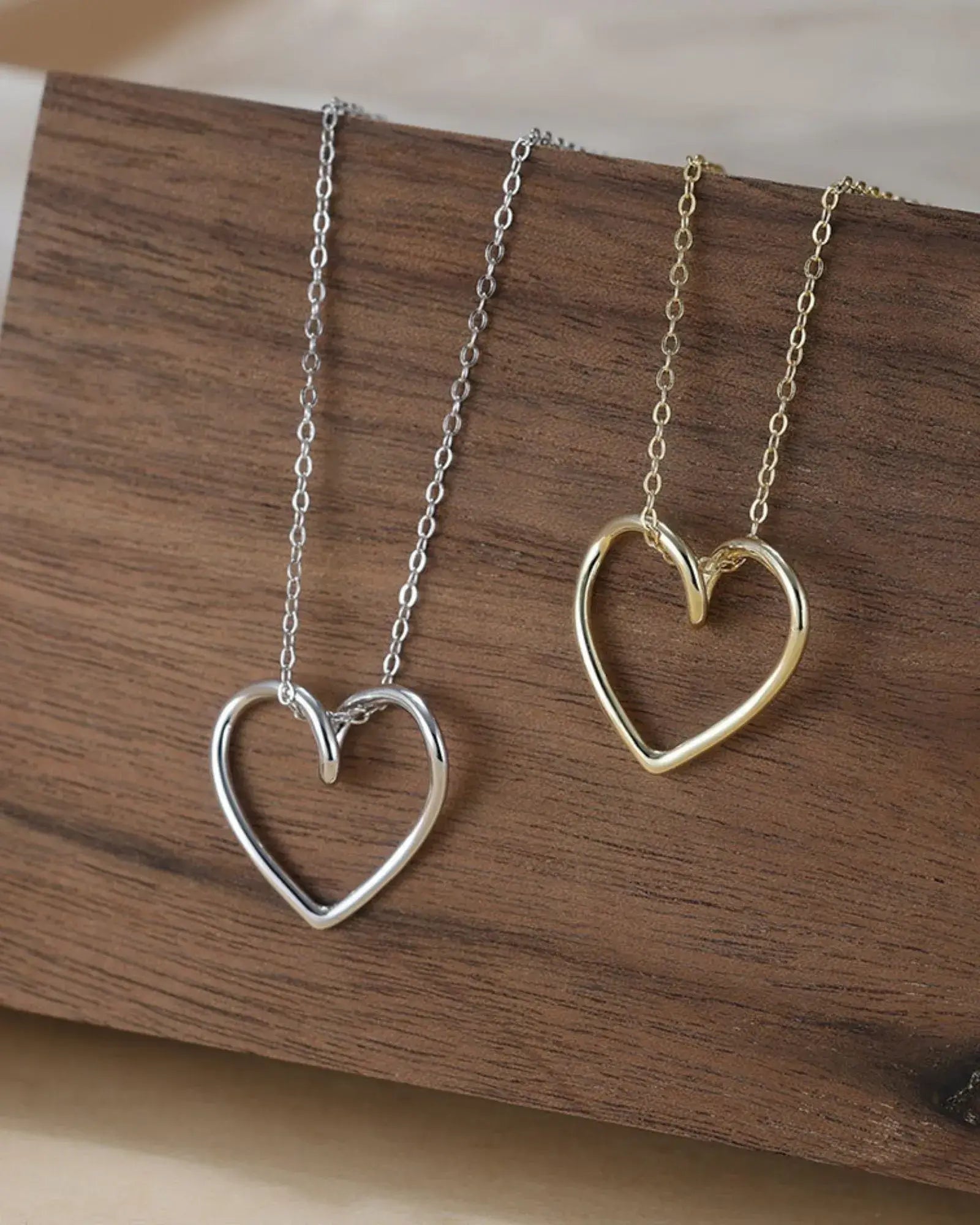 True Heart Pendant Necklace in sterling silver and gold plating, showcasing fluid heart shapes on a wooden display.
