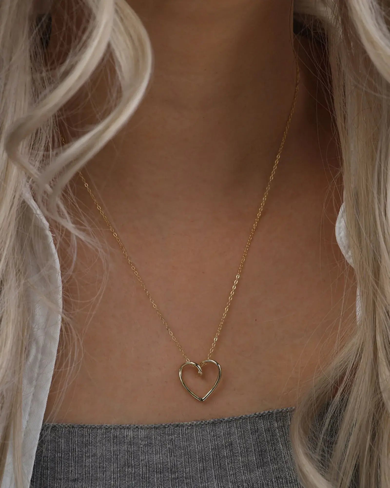 Gold heart pendant necklace elegantly worn against a grey top, showcasing its refined, sculptural design.