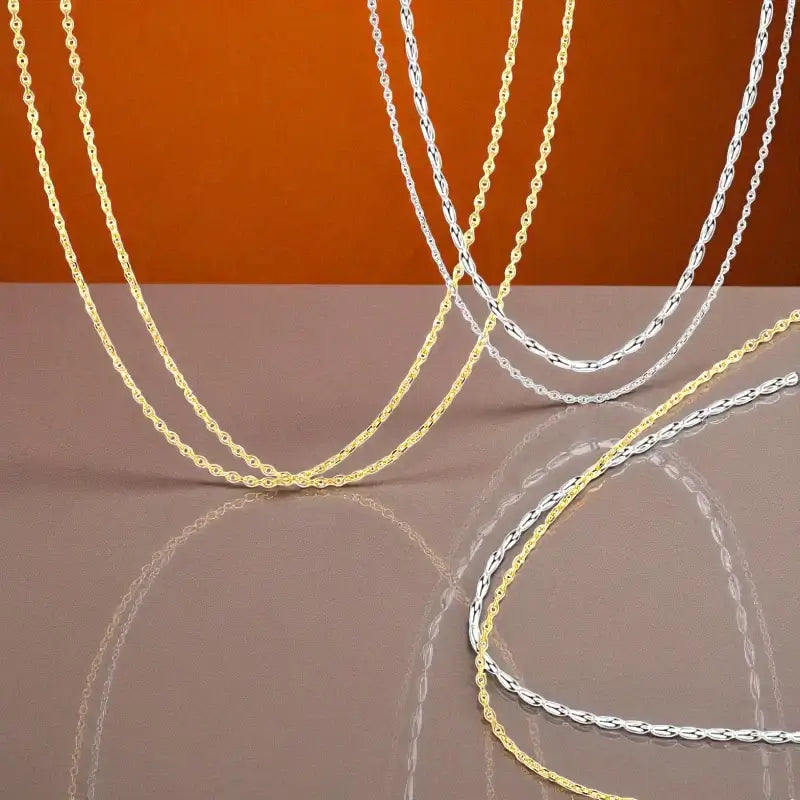 Basic chains in sterling silver and gold displayed elegantly on a reflective surface.
