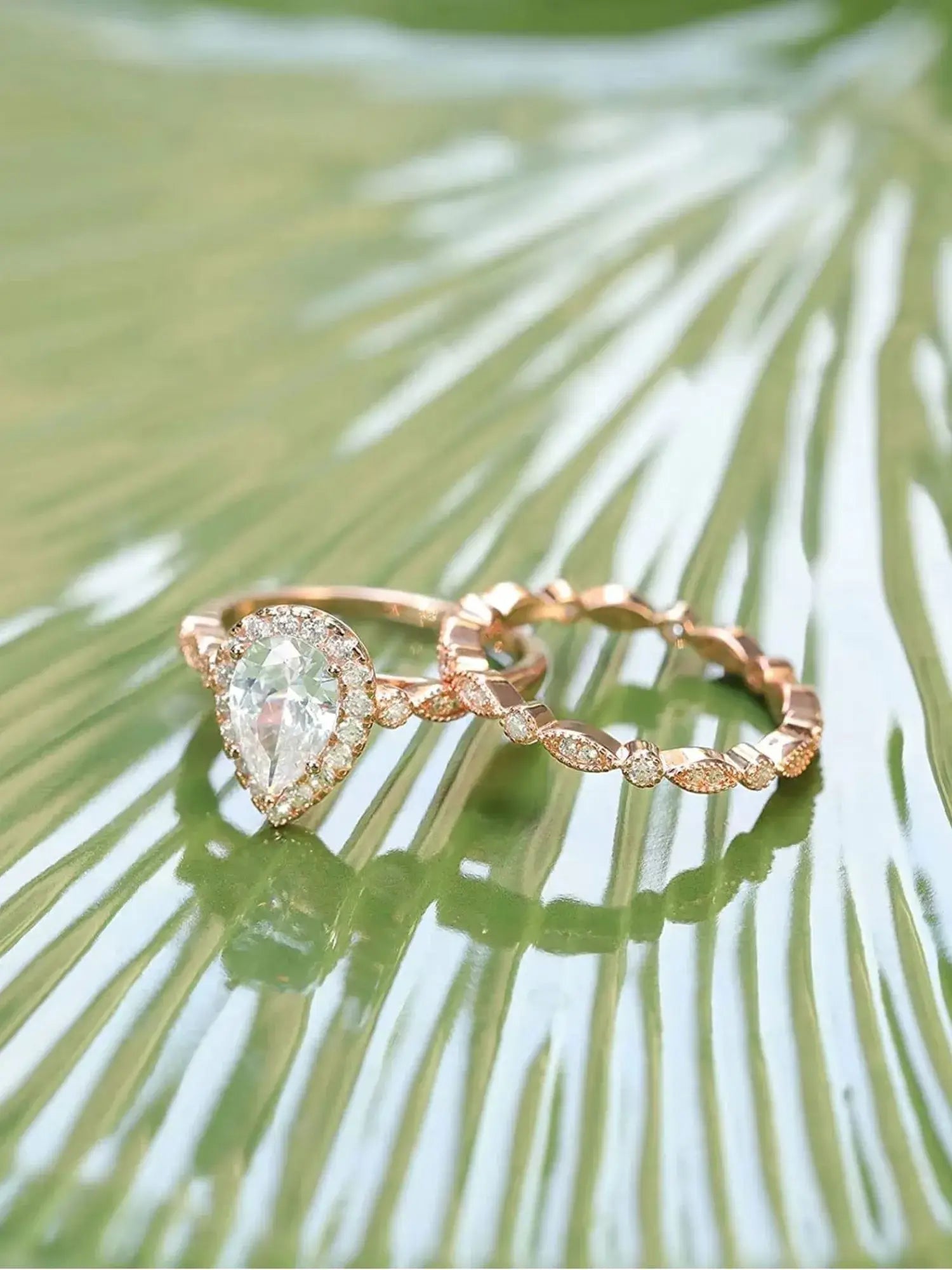 1.5CT teardrop CZ two ring set in rose gold on a green leaf, showcasing its romantic design and sparkling zircon stones.