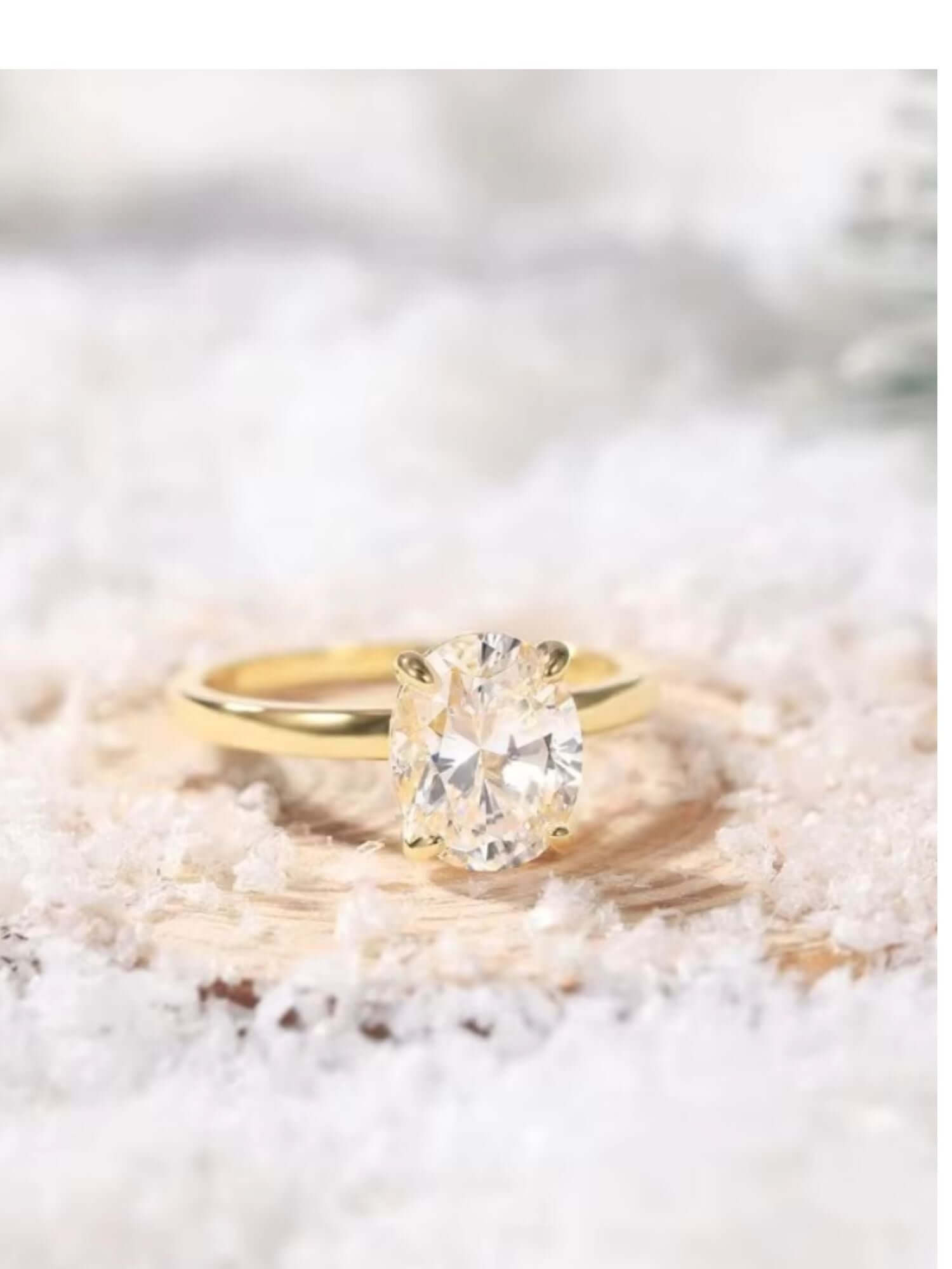 3CT oval cut solitaire cubic zirconia ring in yellow gold setting, resting on white snow.