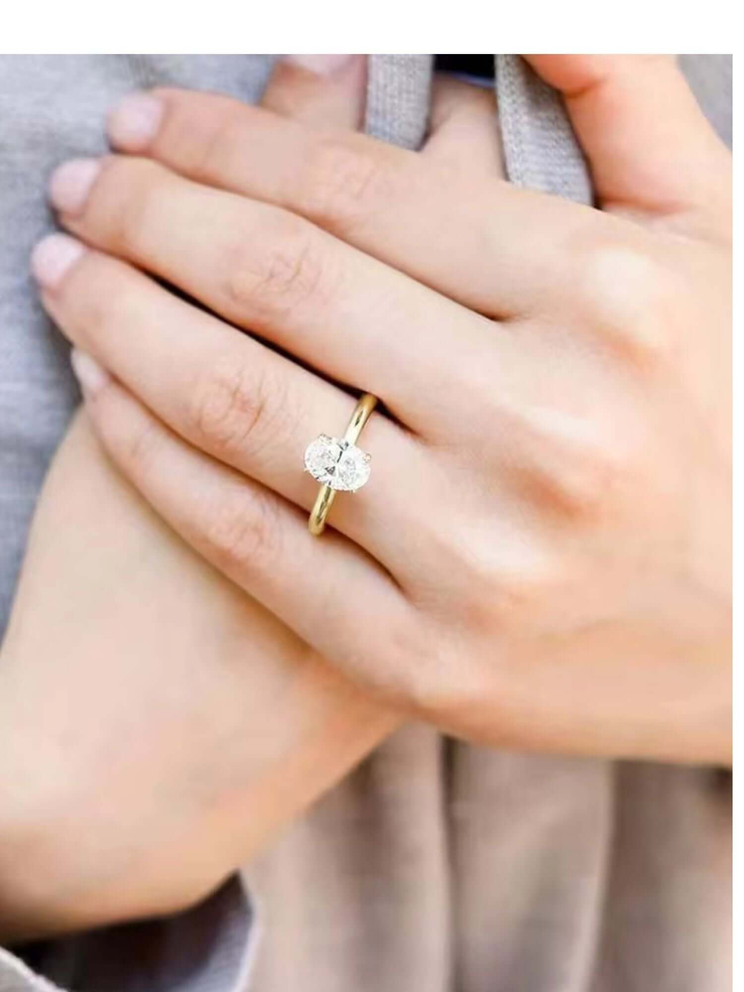 Close-up of a hand wearing a 3CT oval cut solitaire cubic zirconia ring on a polished gold band.
