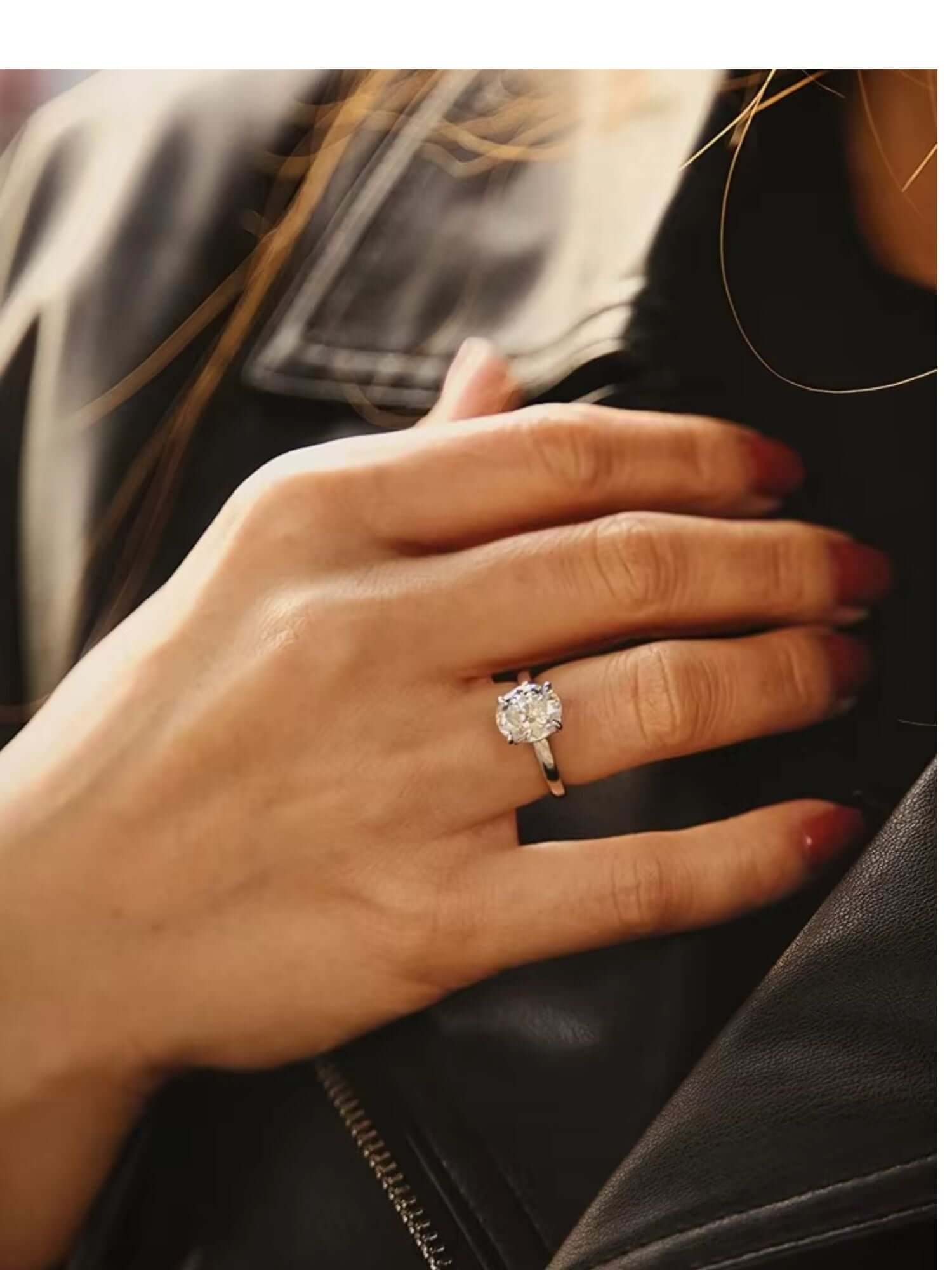 Elegant hand wearing a 3CT oval cut solitaire cubic zirconia ring on a polished band, against a leather jacket background.