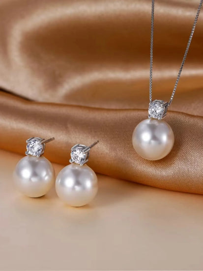 Elegant pearl necklace and earring set with zirconia, displayed on rich satin fabric.