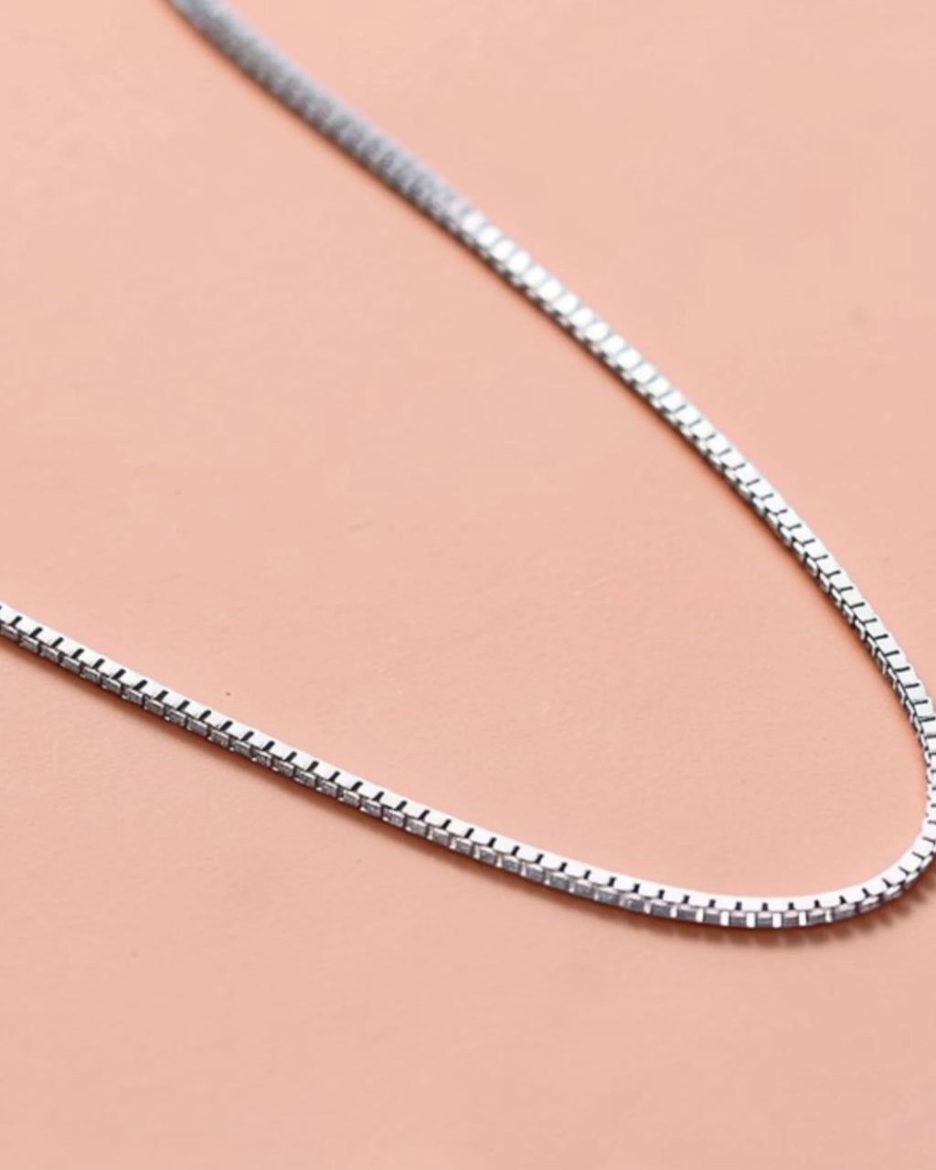 0.6mm Box Chain sterling silver resting on a pink surface, showcasing its sleek design and platinum finish.