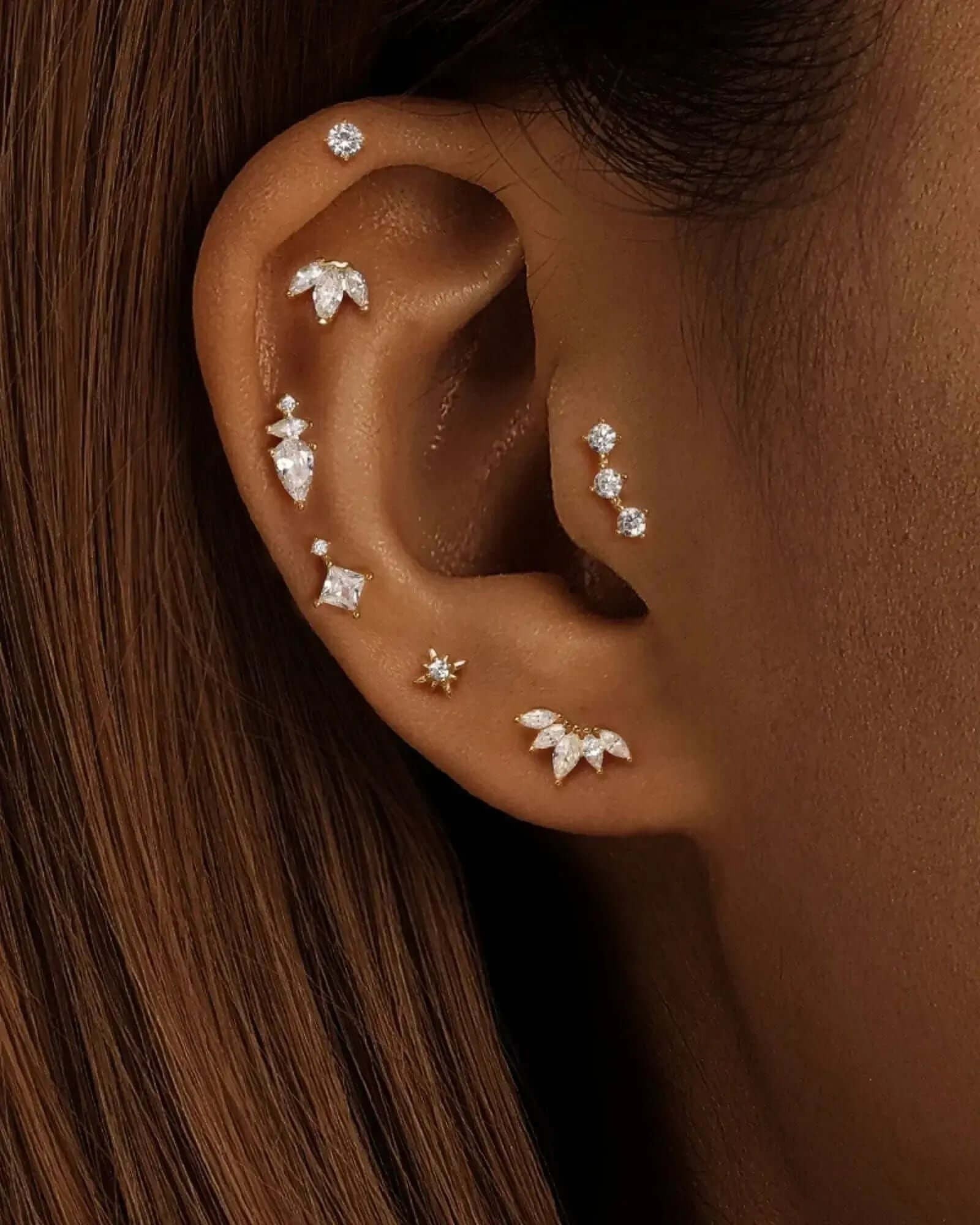 Close-up of multiple ear piercings adorned with sparkling studs and decorative earrings on a model's ear.