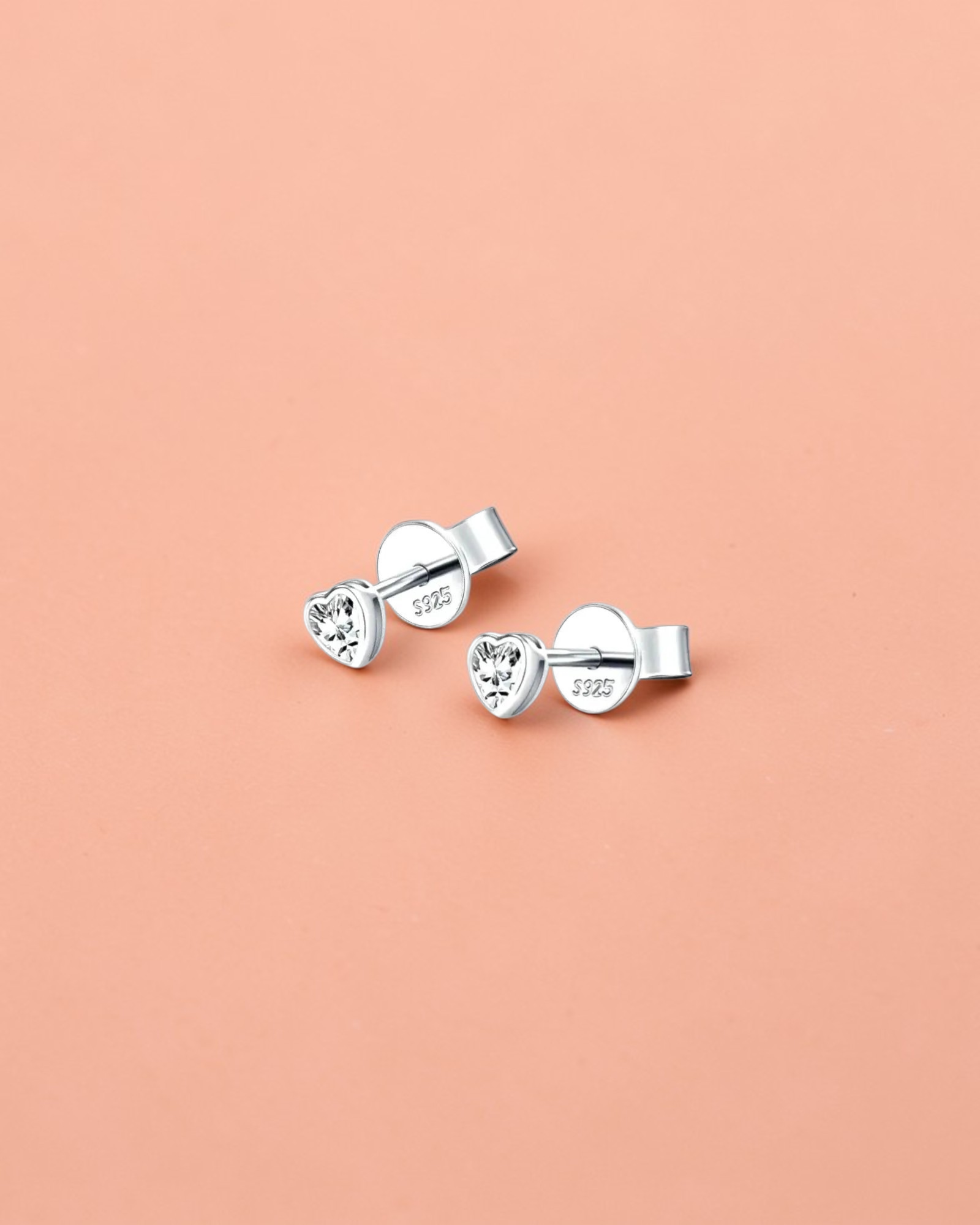 Pair of silver heart-shaped stud earrings on a light gray background