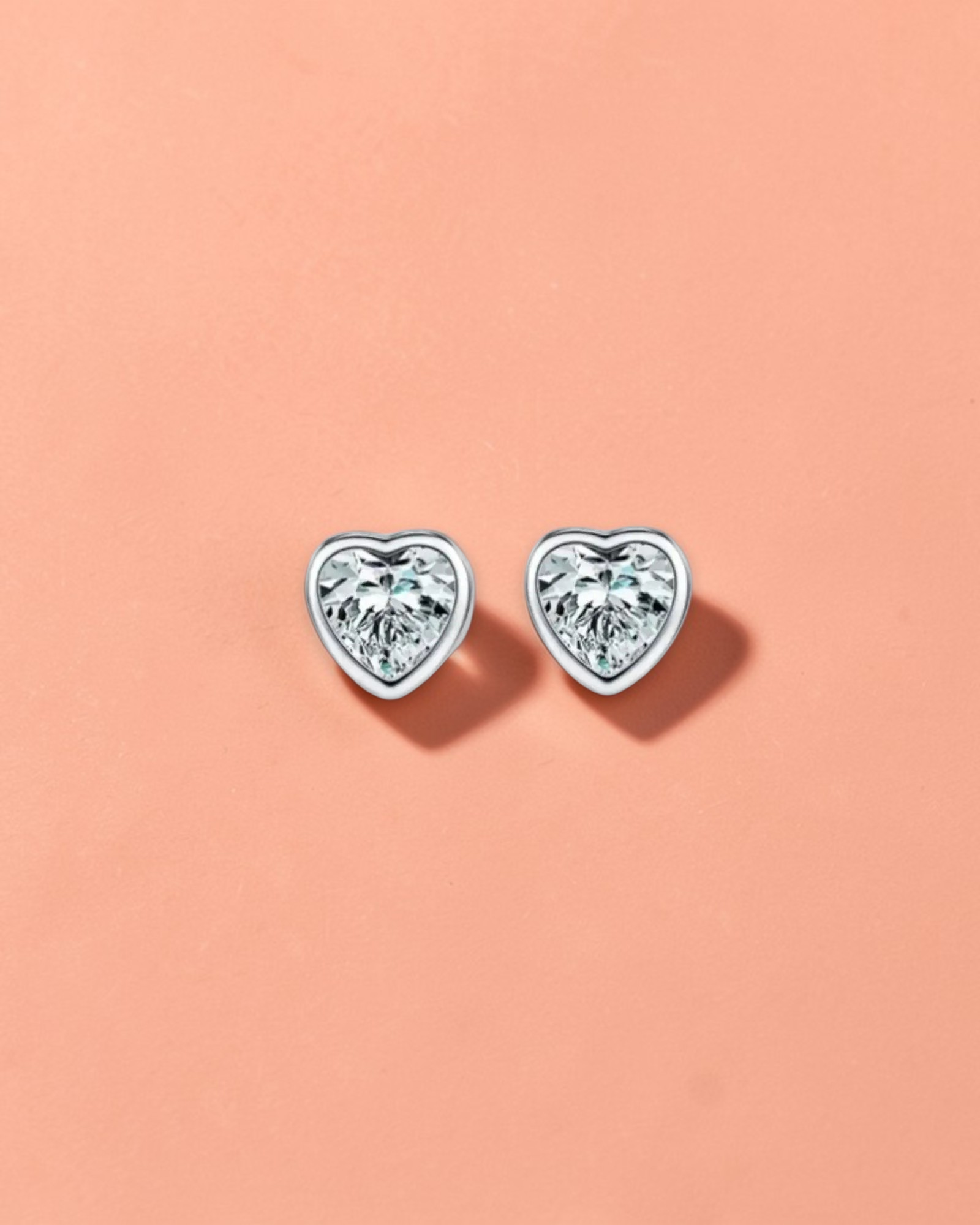 Heart-shaped diamond stud earrings on a light gray background