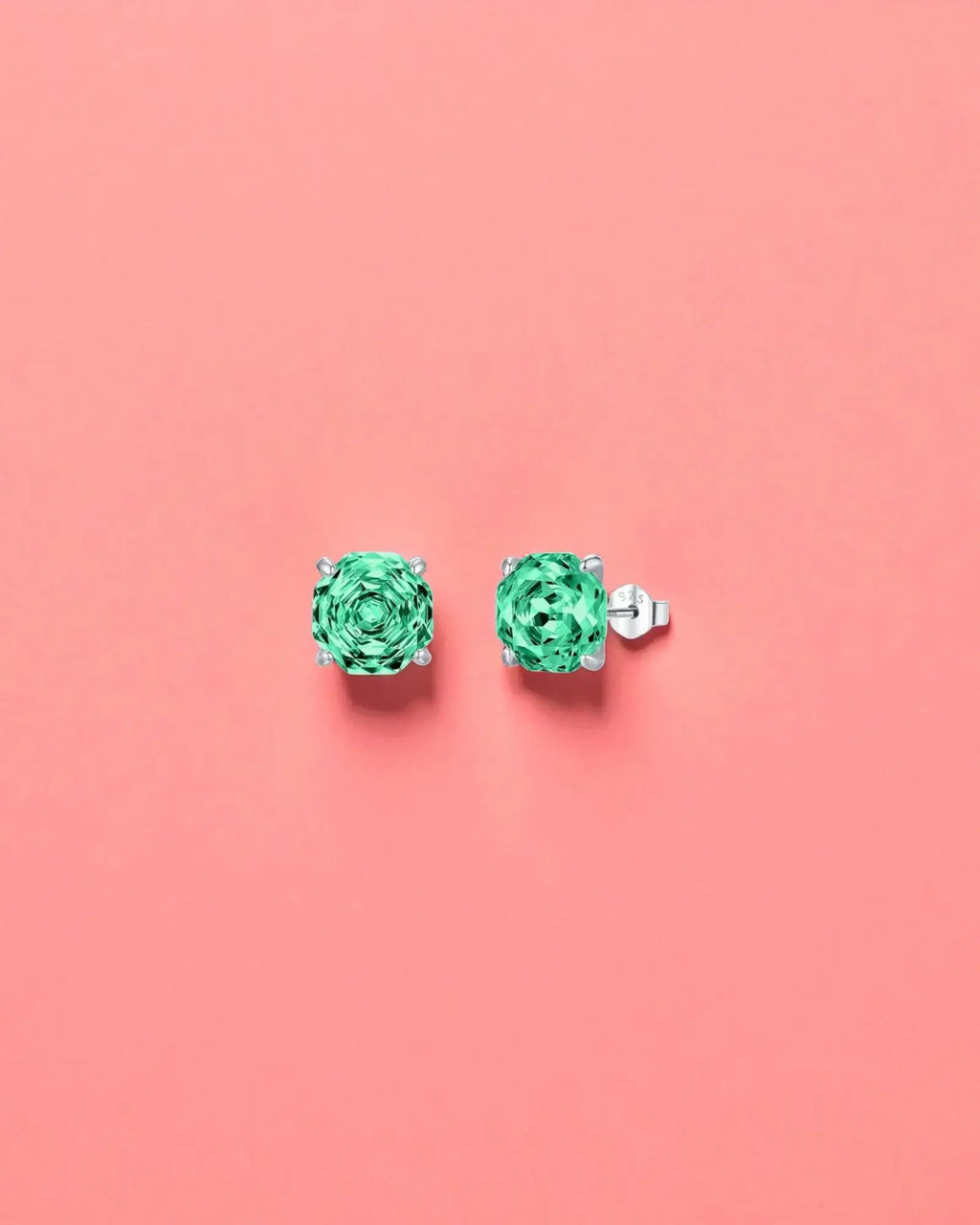 Pair of green gemstone earrings on a pink background