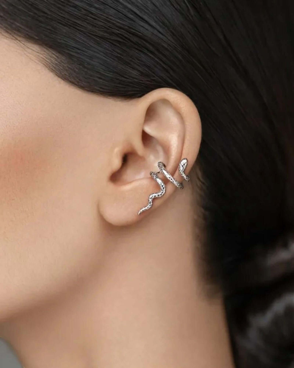 Close-up of an ear wearing a silver earring with dark hair and skin background