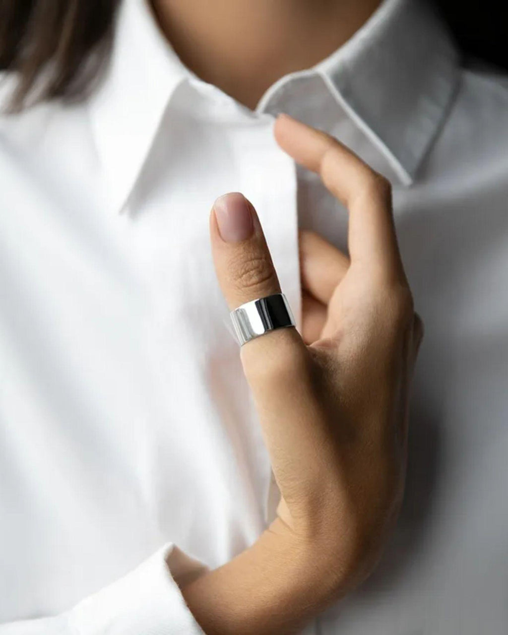 Close-up of a hand wearing a silver ring with a white shirt background
