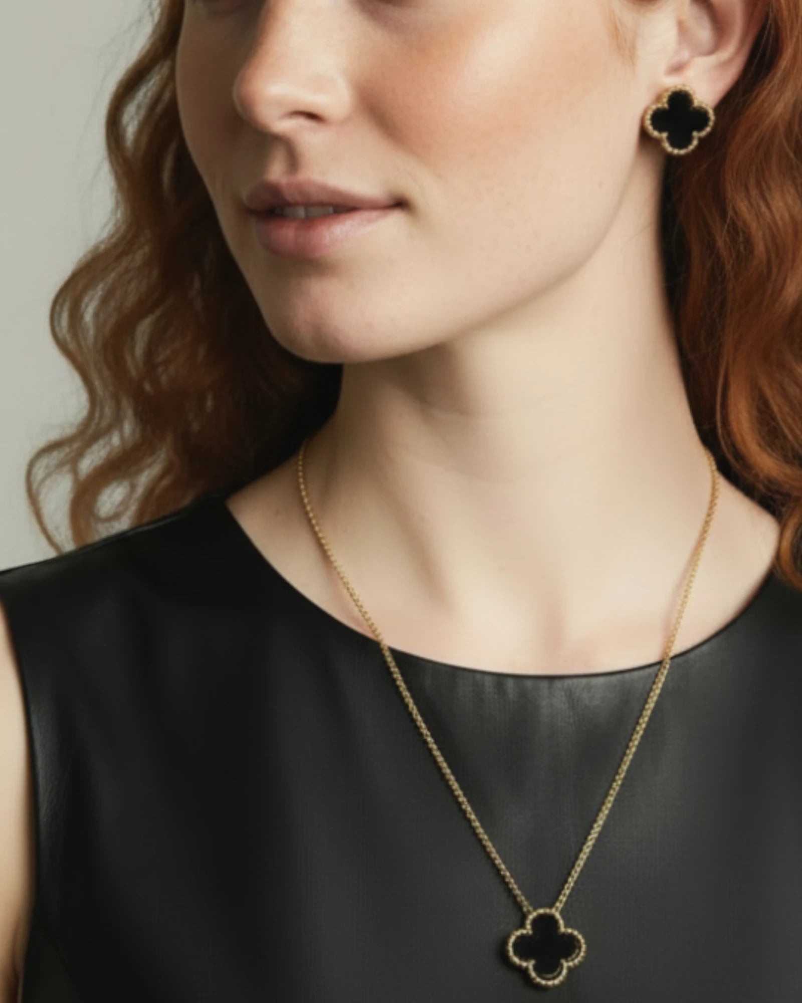 Woman wearing a gold necklace with a clover-shaped pendant and matching earrings.