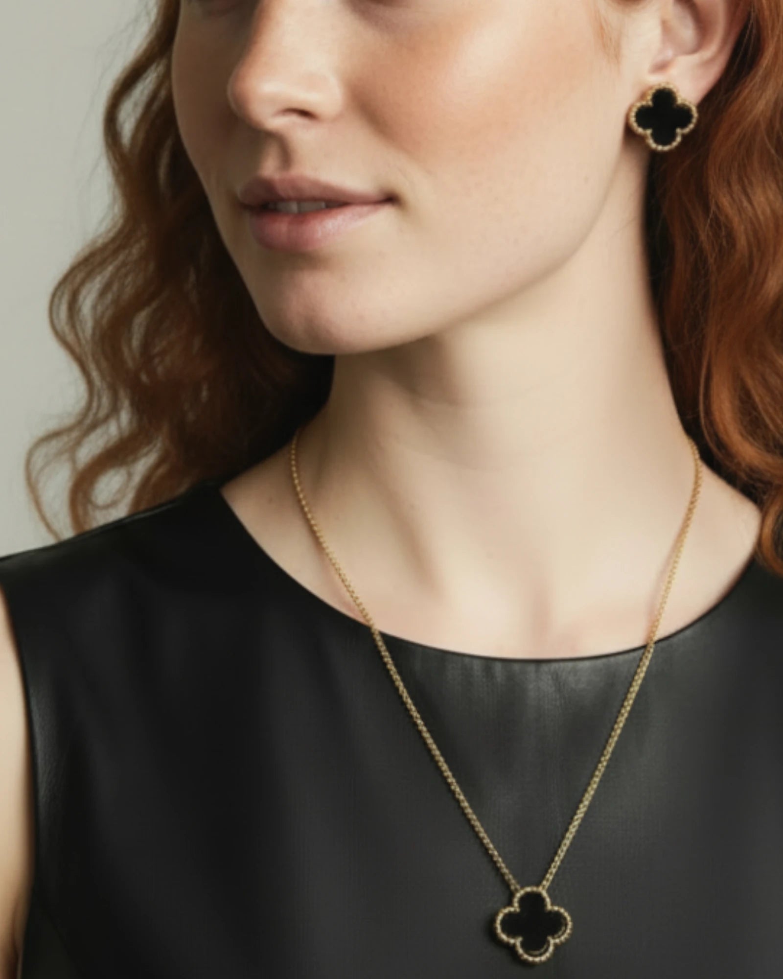 Woman wearing a gold necklace with a clover-shaped pendant and matching earrings.
