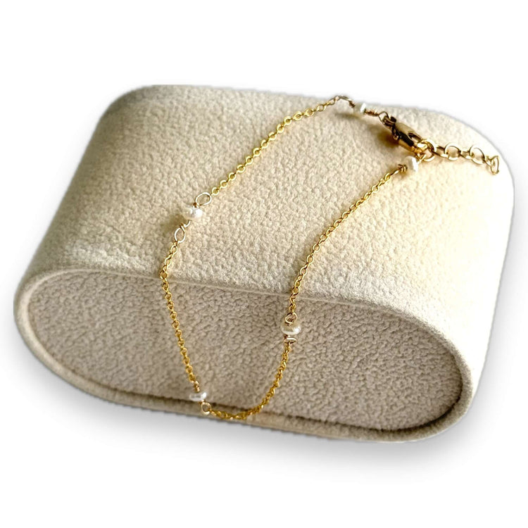 A dainty pearl bracelet made in gold filled is displayed over a velvet bracelet display block