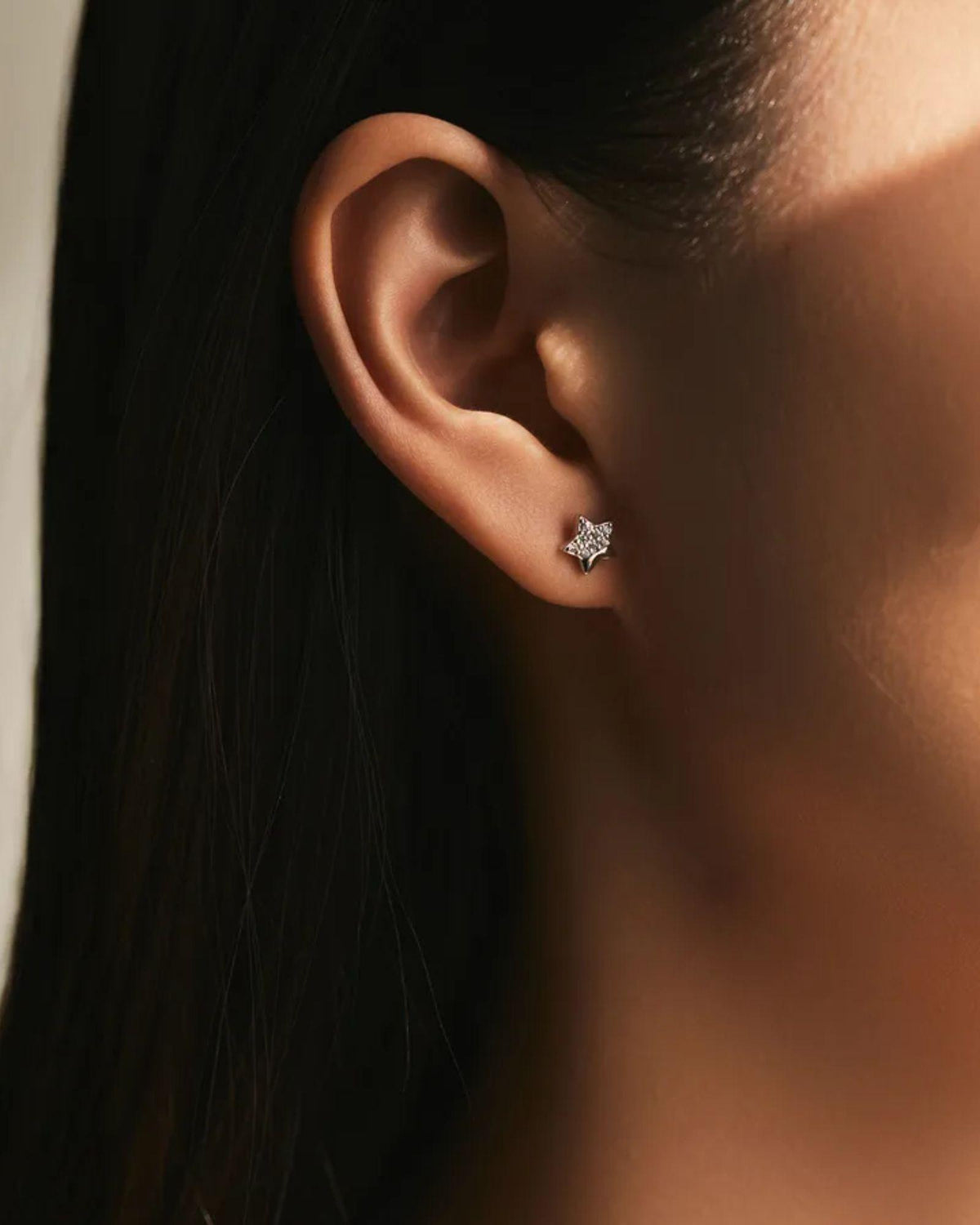 Close-up of an ear wearing a diamond earring with a blurred background