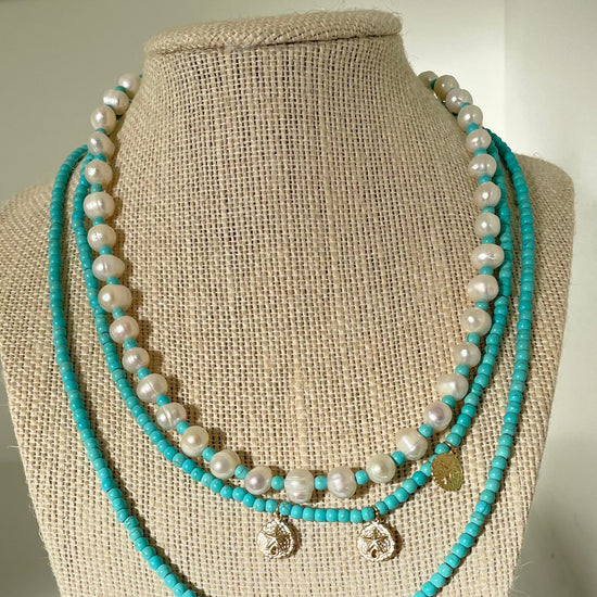 A beautiful beaded pearl and turquoise necklace displayed in a necklace stand with other necklaces