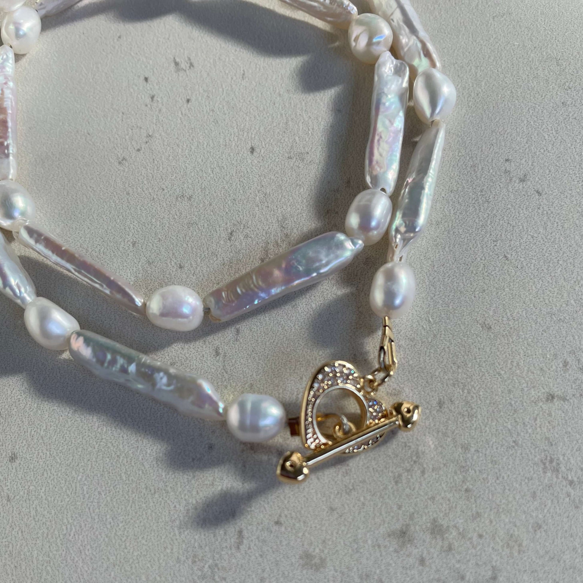 a close up look of a pearl necklace with heart toggle clasp.