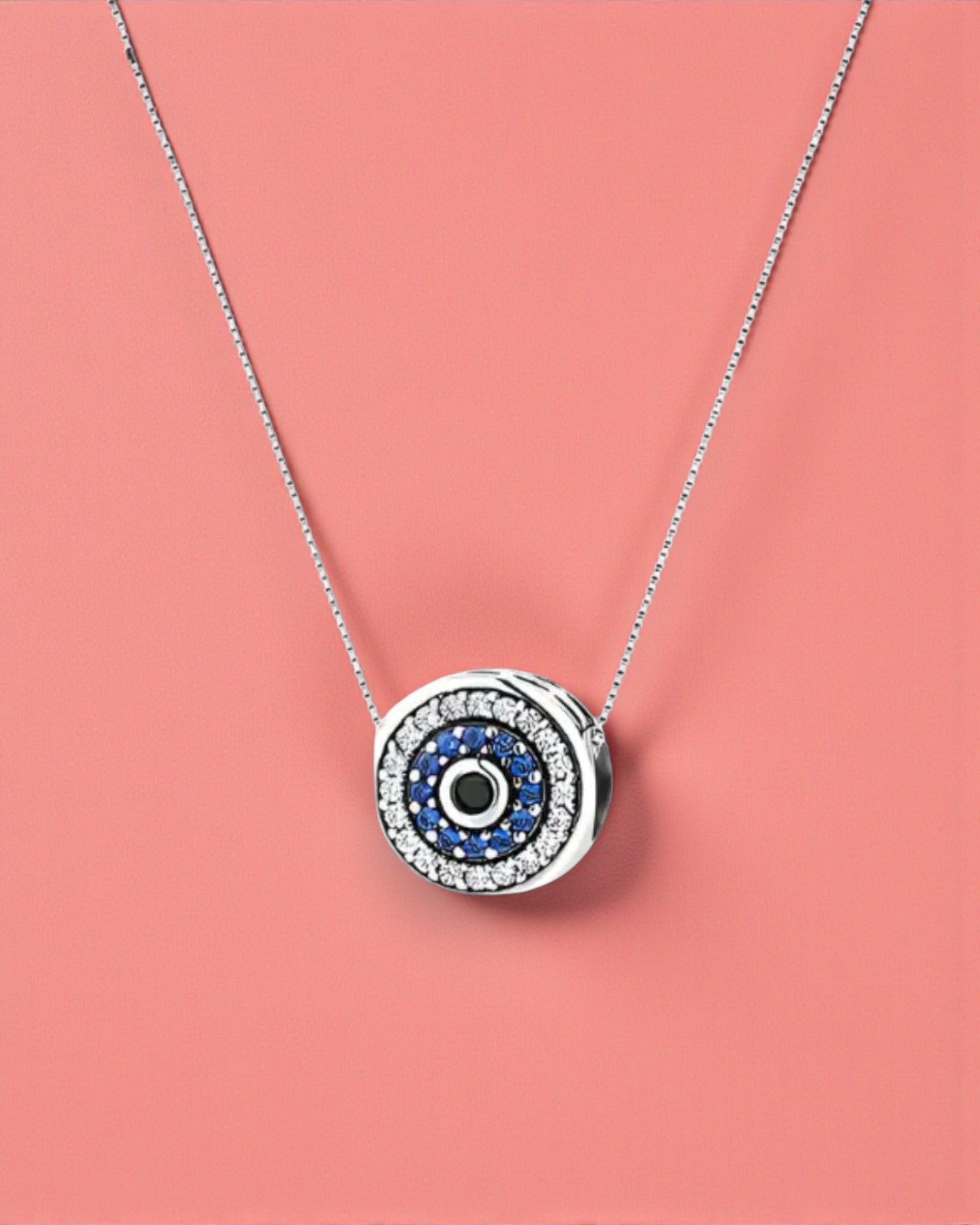 Silver necklace with a round pendant featuring blue and black stones on a pink background